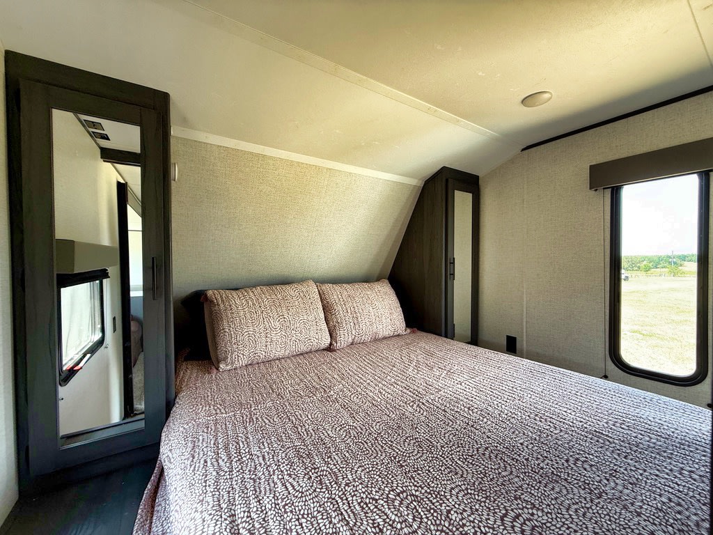 Comfortable RV rental bedroom with queen bed, built-in storage, and bright window for travel adventures.. Aspen Trail LE 2021