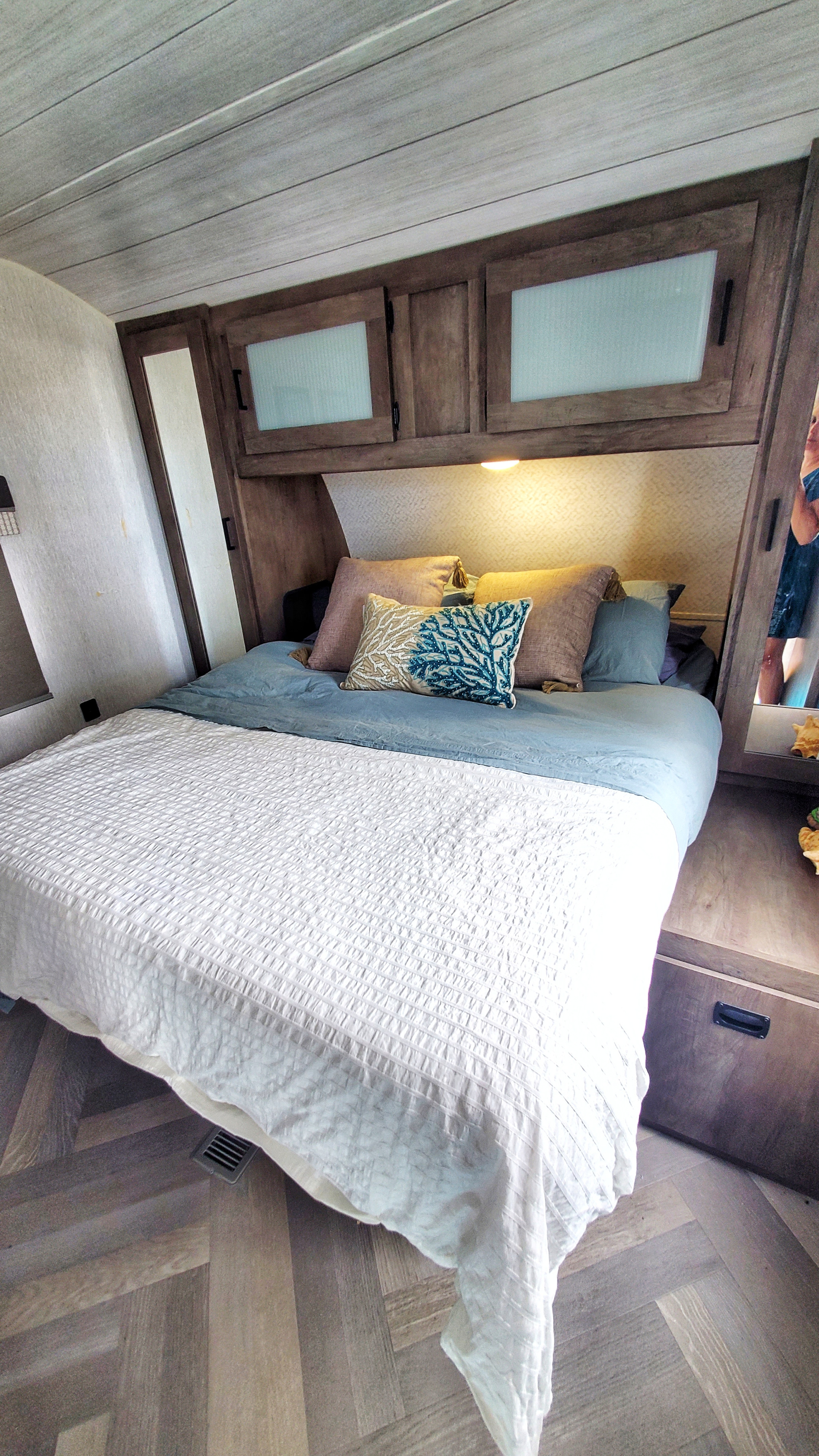Experience comfort in this RV rental bedroom, featuring a bed with pillows, overhead cabinets, and herringbone wood-look flooring.. Forest River Salem 2022
