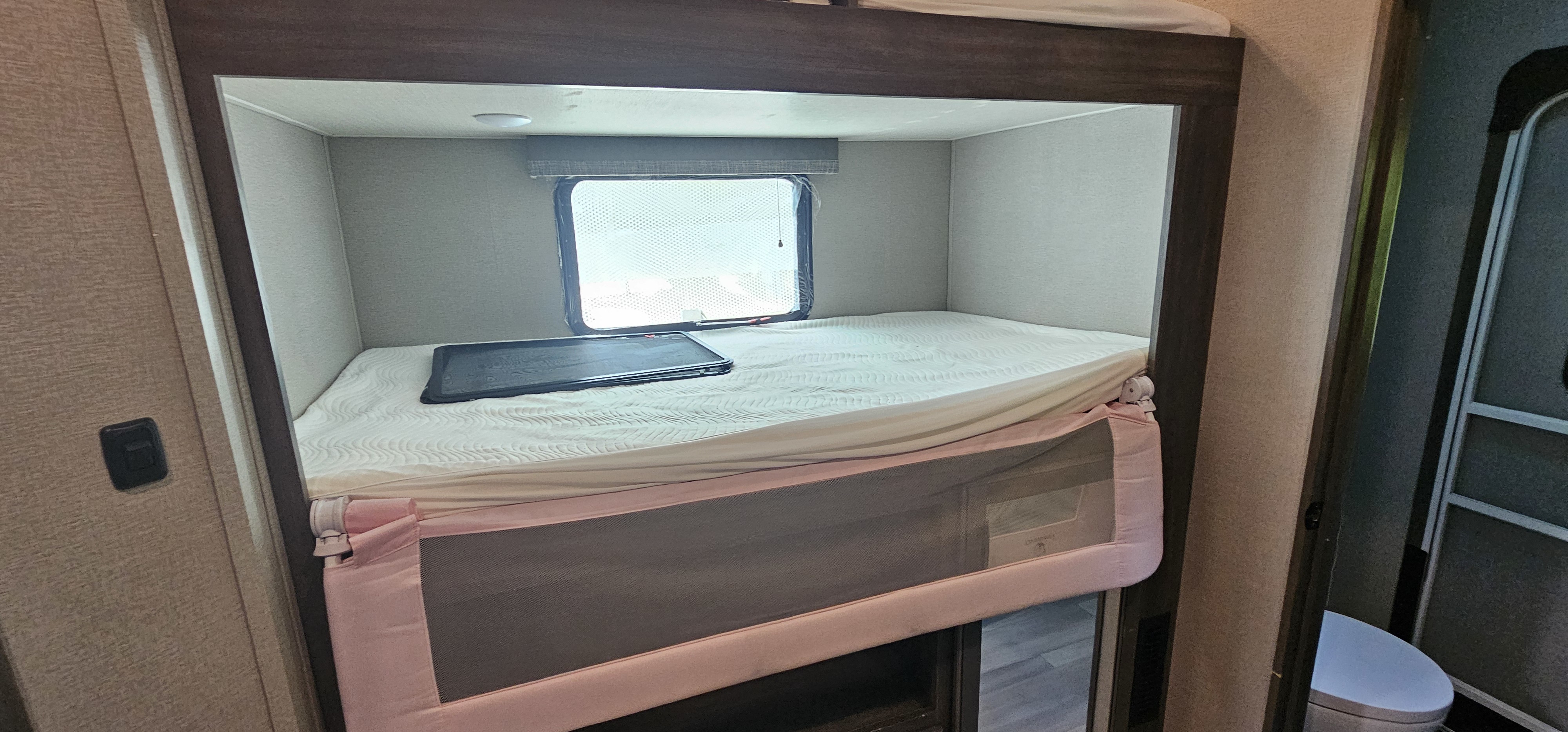 This RV rental features a cozy bunk bed with a window, safety rail, and comfy mattress, ideal for sleeping.. Grand Design Solitude S-Class 2022