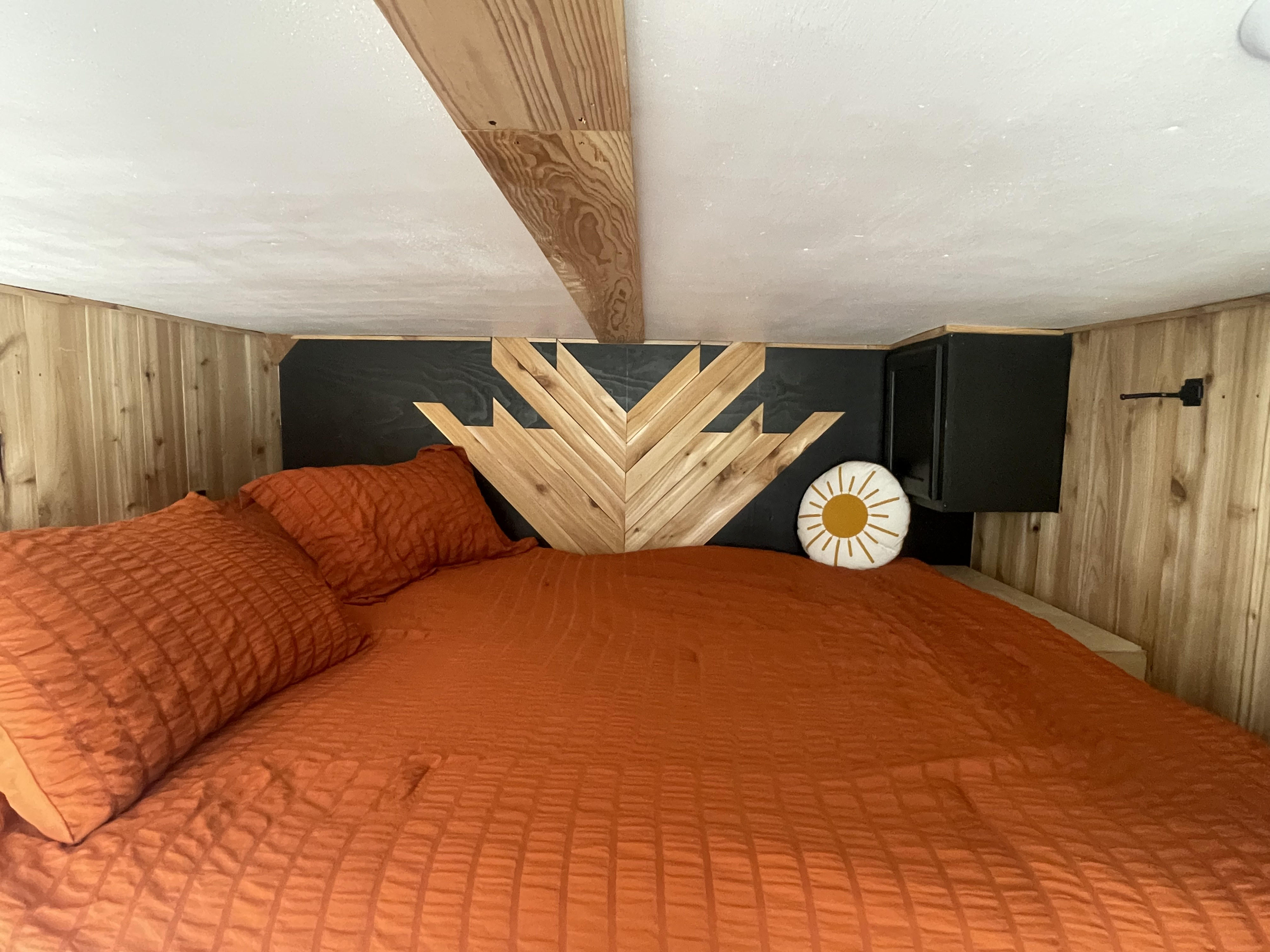 Cozy RV rental bedroom loft featuring an orange bed, geometric wood headboard, and wood paneling.. Ford F350 1999