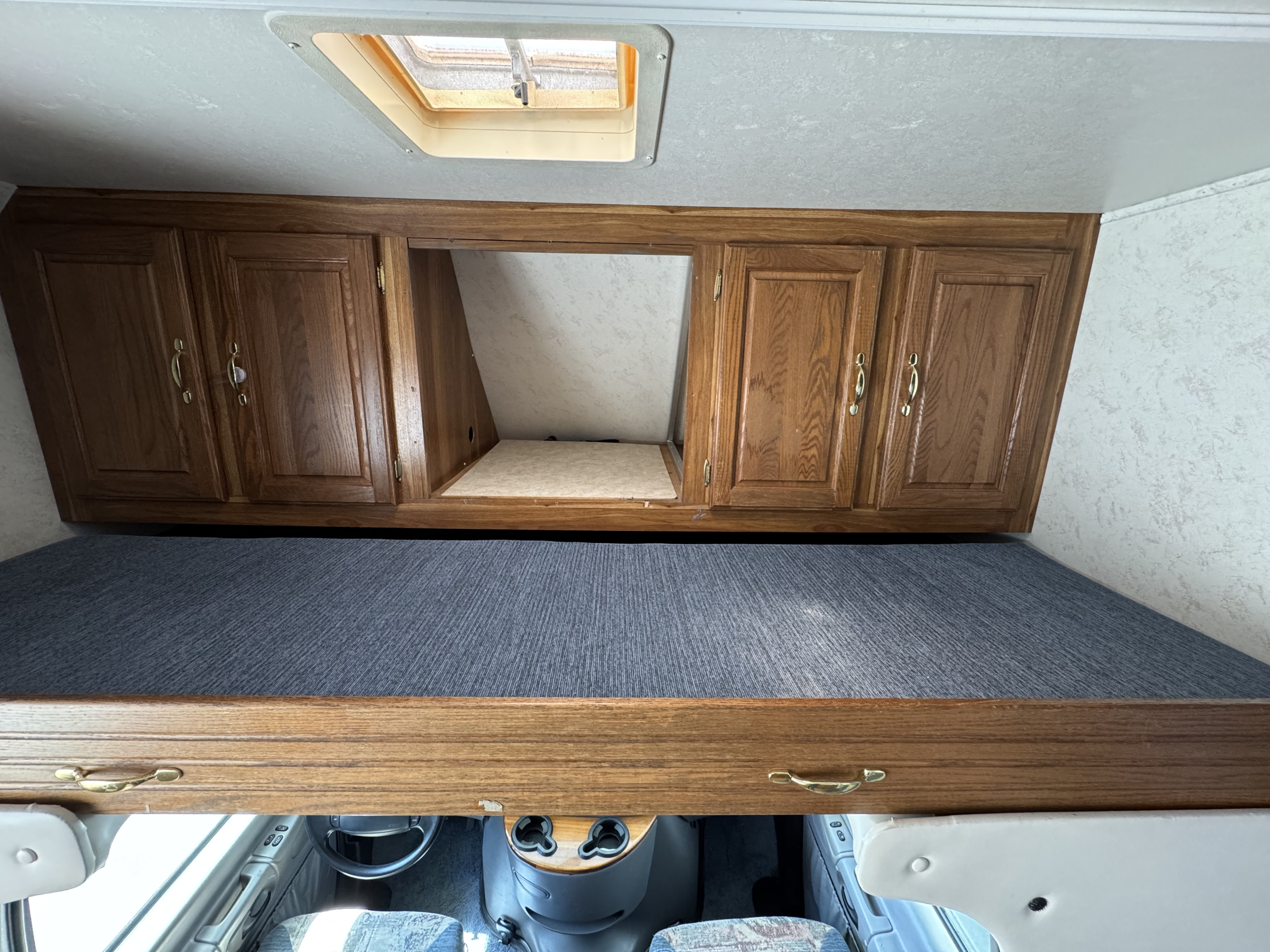 RV rental interior: Overhead wooden cabinets, cab-over bunk bed with gray carpet, and a skylight.. Thor Motor Coach Four Winds 1999