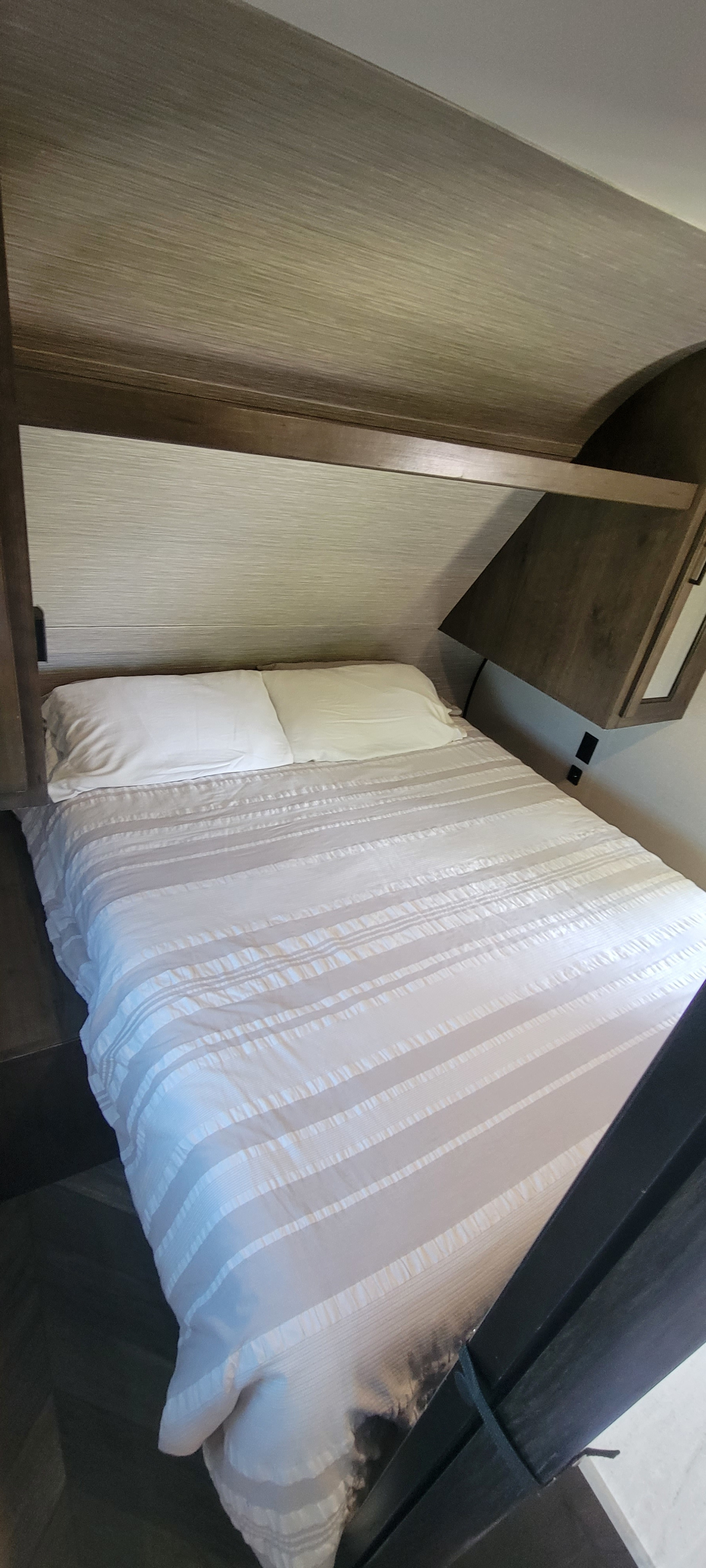 RV rental bedroom: a neat bed with striped bedding, textured headboard, and compact overhead storage.. Highland Ridge RV Olympia 2022