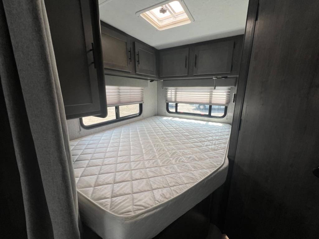 RV rental interior: Clean bed, overhead cabinets, and windows in a compact bedroom. Ready for your adventure.. Coachman Leprechaun 2022