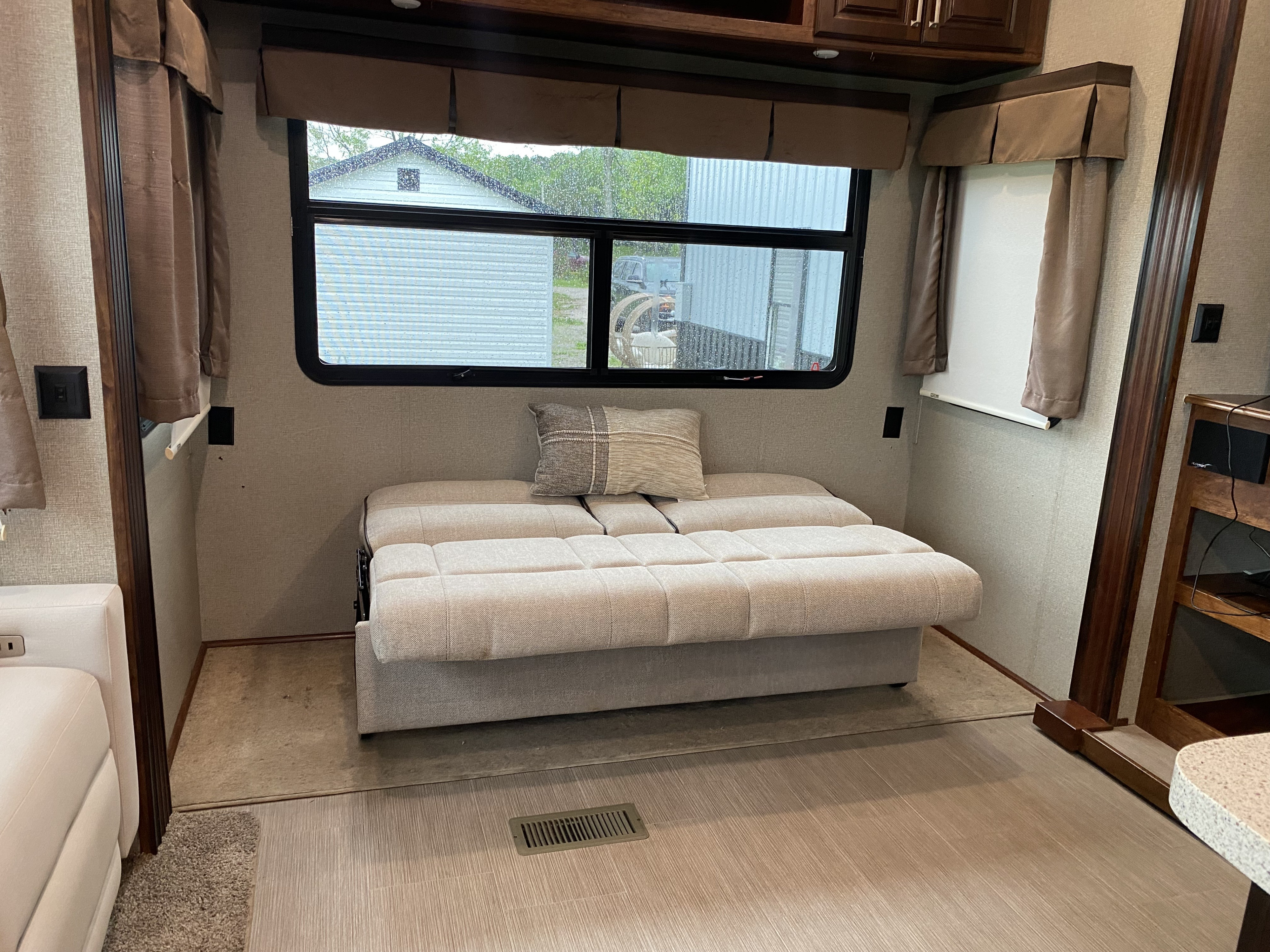 Cozy RV rental living area featuring a sofa bed, large window with a rainy outdoor view, and modern interior design.. Keystone RV Avalanche 2017