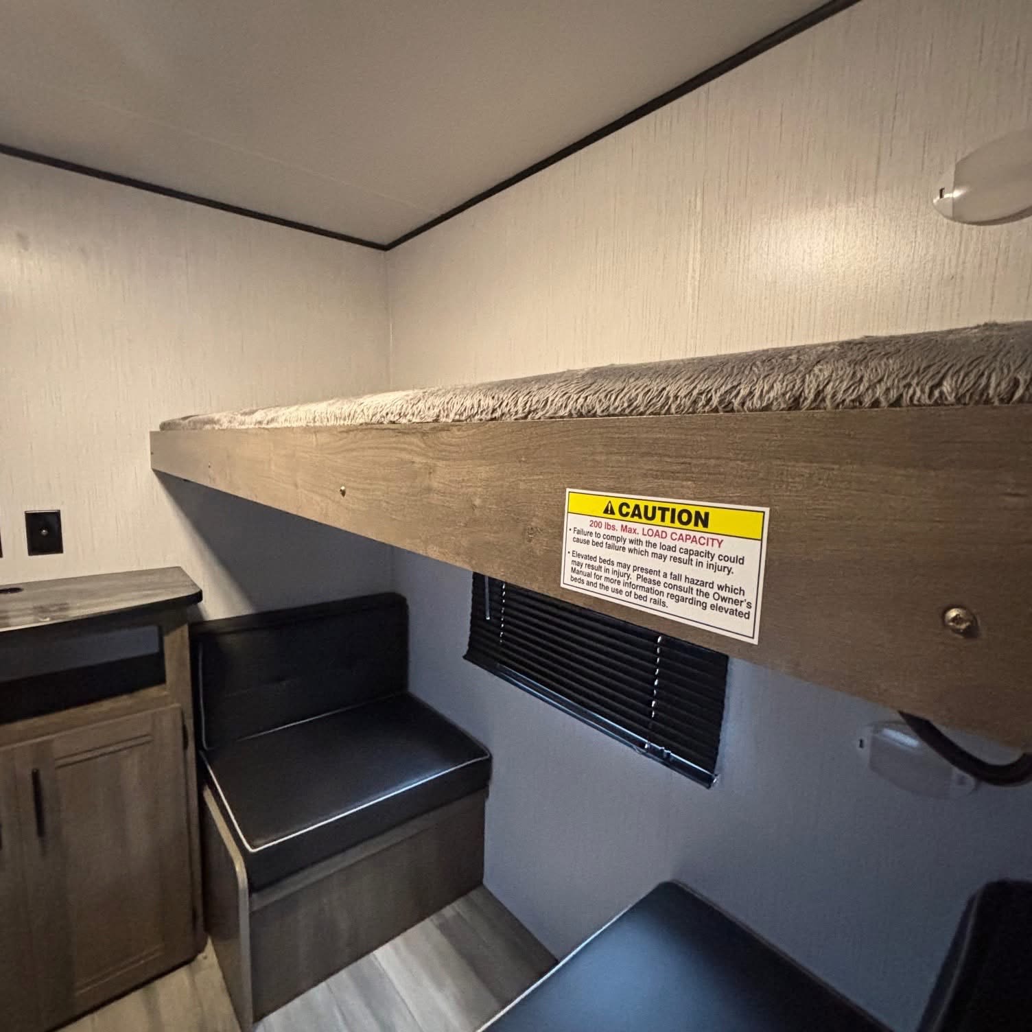 Inside an RV rental: a cozy bunk bed with a 200 lb. max capacity, plus compact seating and a small cabinet area.. Heartland RVs Pioneer 2023