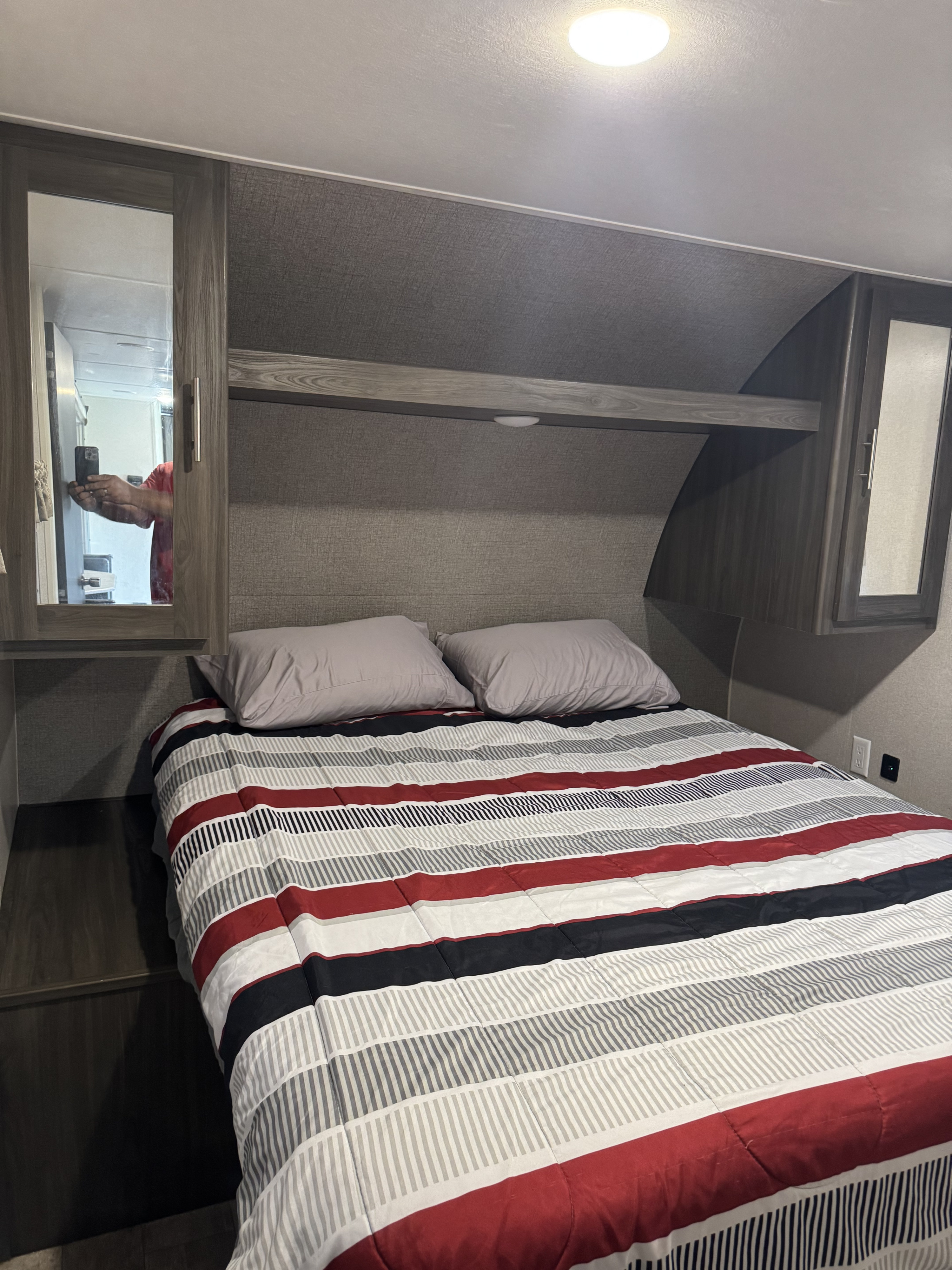 Modern RV rental bedroom featuring a striped bed, pillows, overhead storage, and mirrored cabinets.. Forest River Shasta 2020