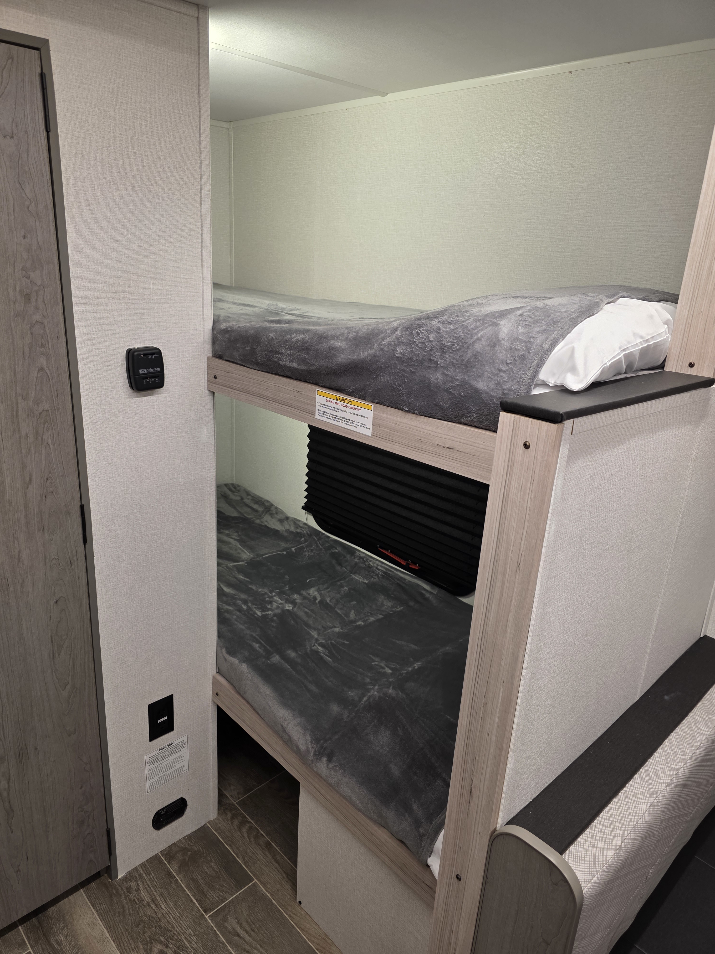Bunk beds with grey blankets in an RV rental interior, showing a caution label & thermostat. Compact sleeping for trips.. Heartland Mallard Switch 2025