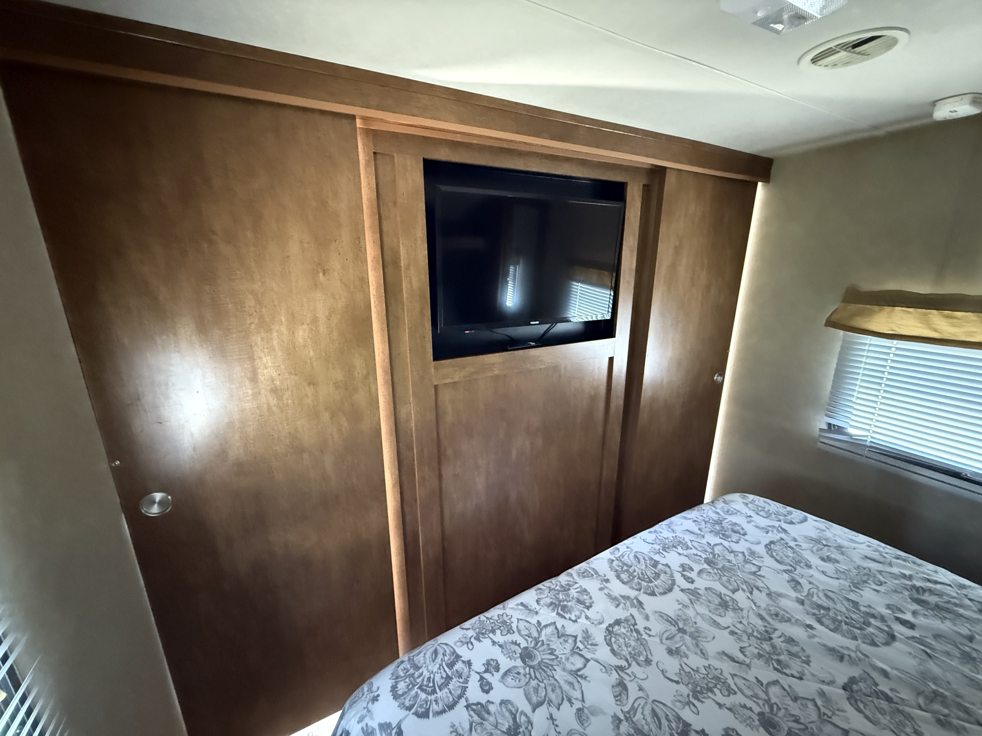This rv rental features a cozy bedroom with a built-in TV, sliding wooden cabinets, and a patterned bed.. Forest River Wildwood 2016
