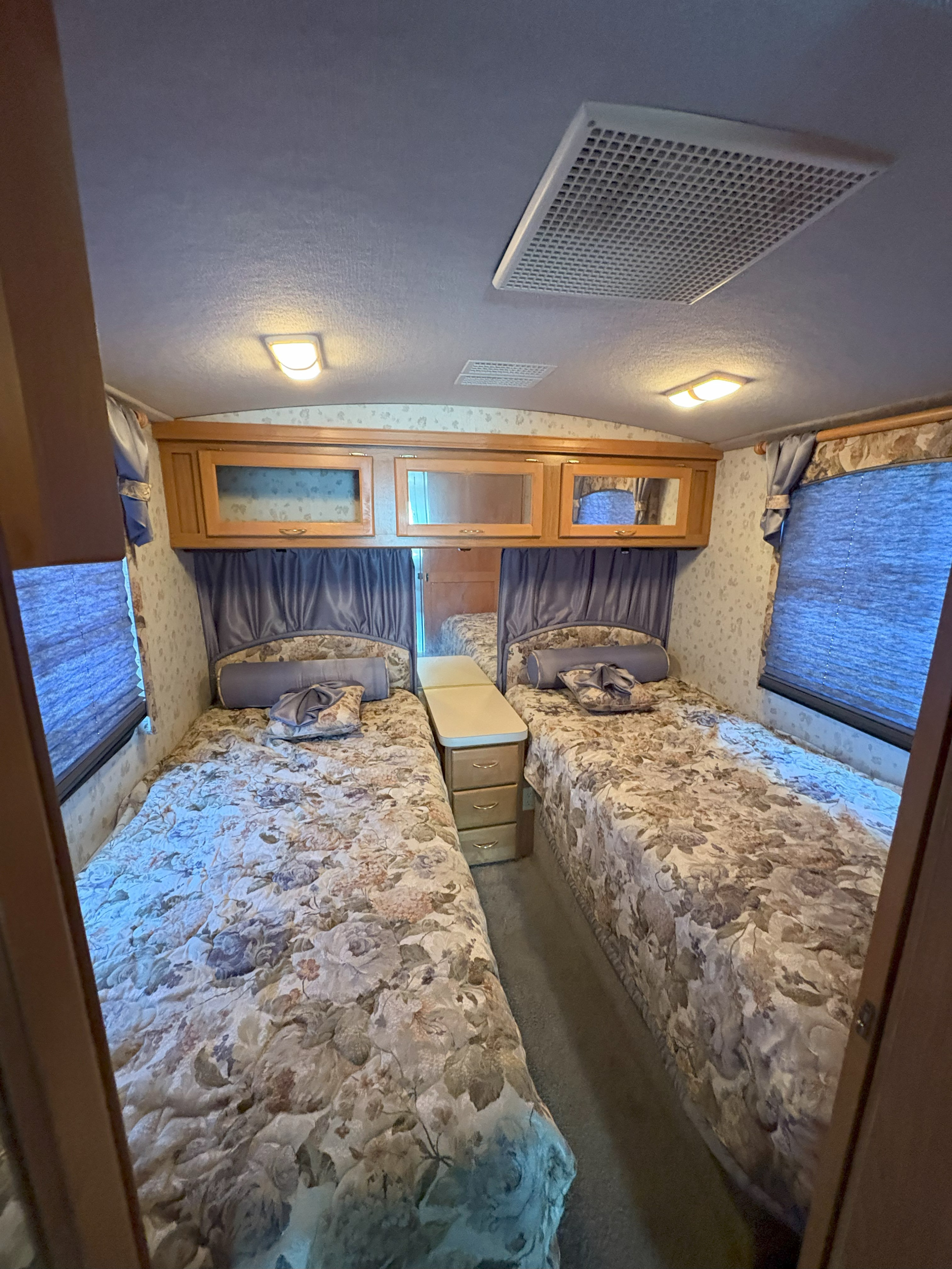 RV rental bedroom with two patterned twin beds, a center nightstand, and overhead wooden cabinets.. Fleetwood Southwind 1998