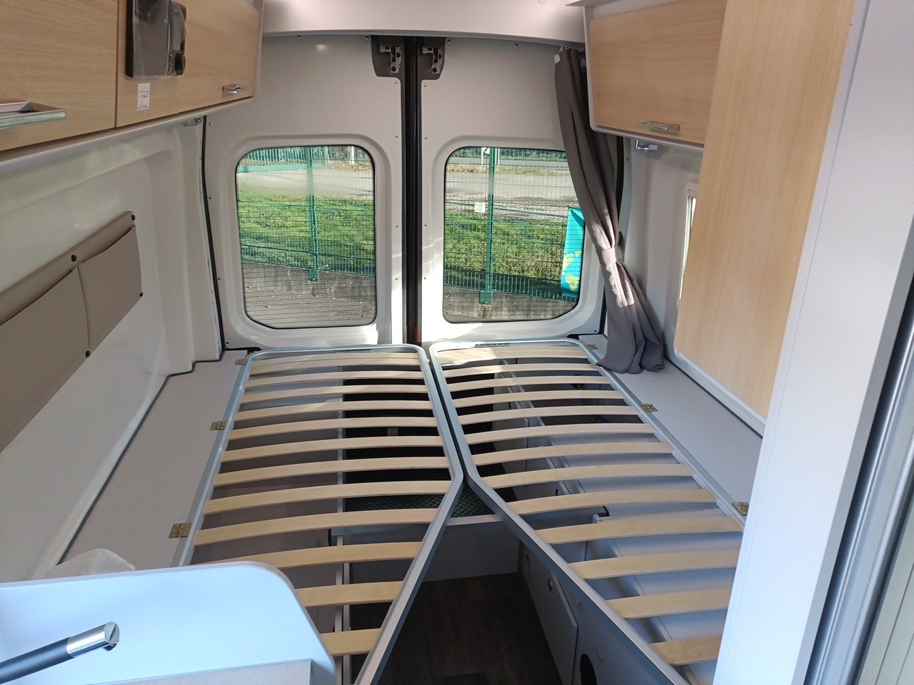 RV rental interior: Rear view showing two slatted bed frames, under-bed storage, overhead cabinets, and back windows.. Font Vendôme Fortyvan Duo 4X4 2023