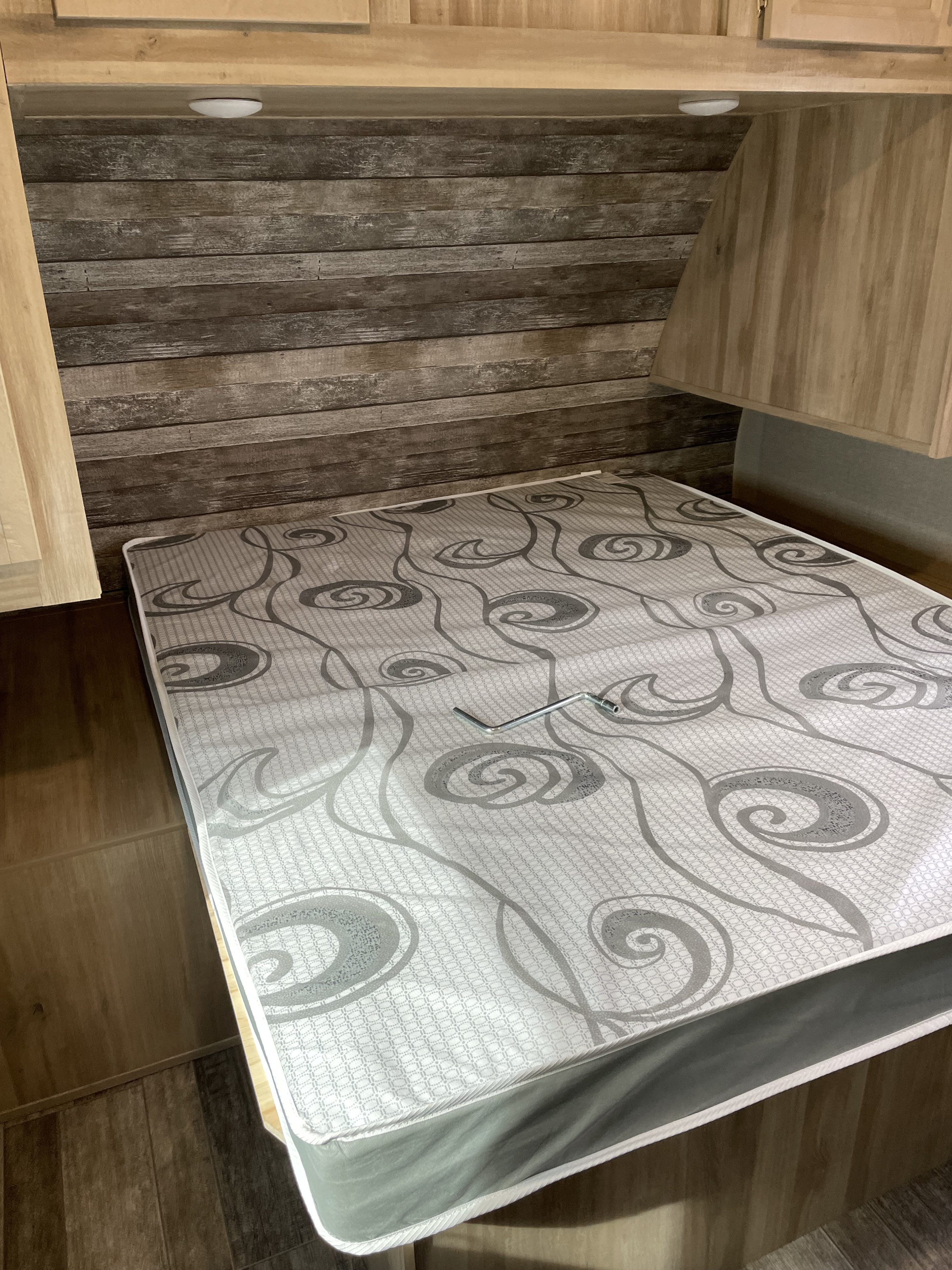 This RV rental bedroom features a patterned mattress on the bed, a rustic wood headboard, and convenient overhead storage.. Coachmen Catalina 263 bhsck legacy edition 2021