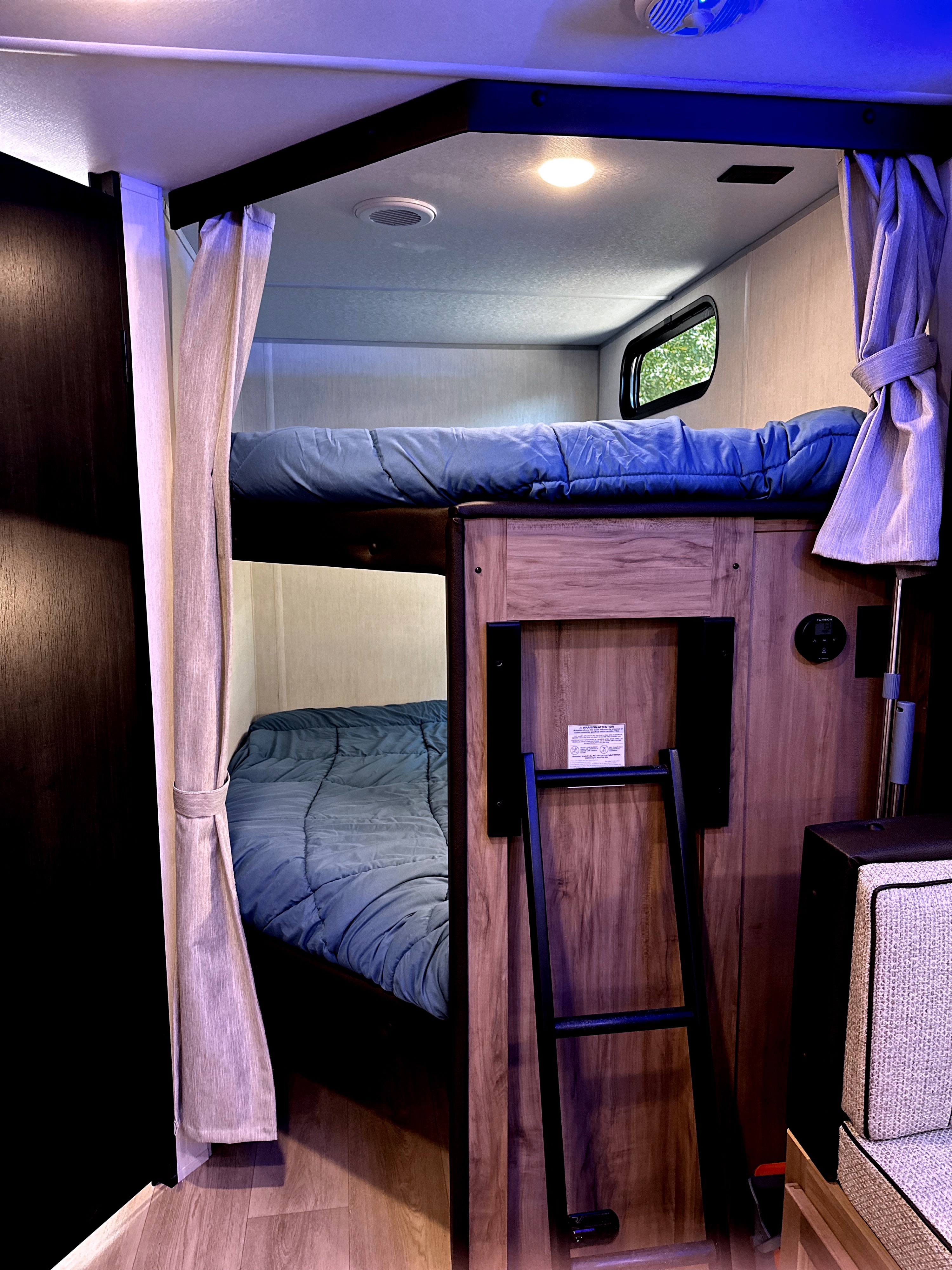 This RV rental bunk bed area features two cozy bunks with blue bedding, a ladder, and privacy curtains.. Forest River Cherokee Black Label 2025