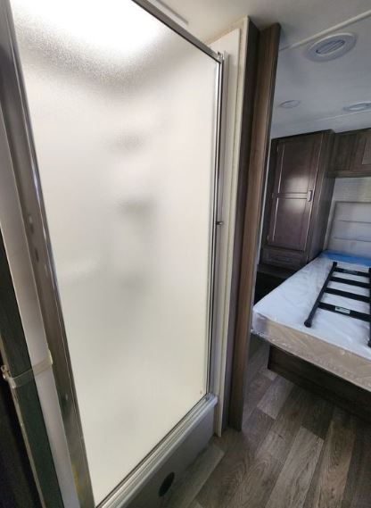 Inside an RV rental: View from the shower entrance into a compact bedroom with a bed, ladder, and wood cabinets.. Winnebago Spirit 2023