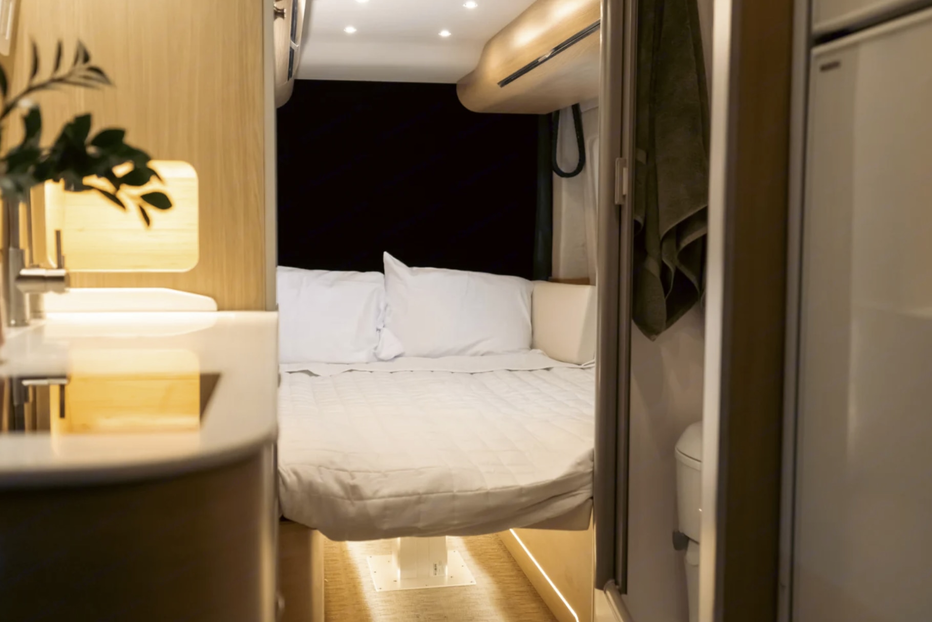 Inside a modern rv rental: A well-appointed sleeping area with white bedding, adjacent sink, and compact bathroom.. Dodge Ram Promaster 2025