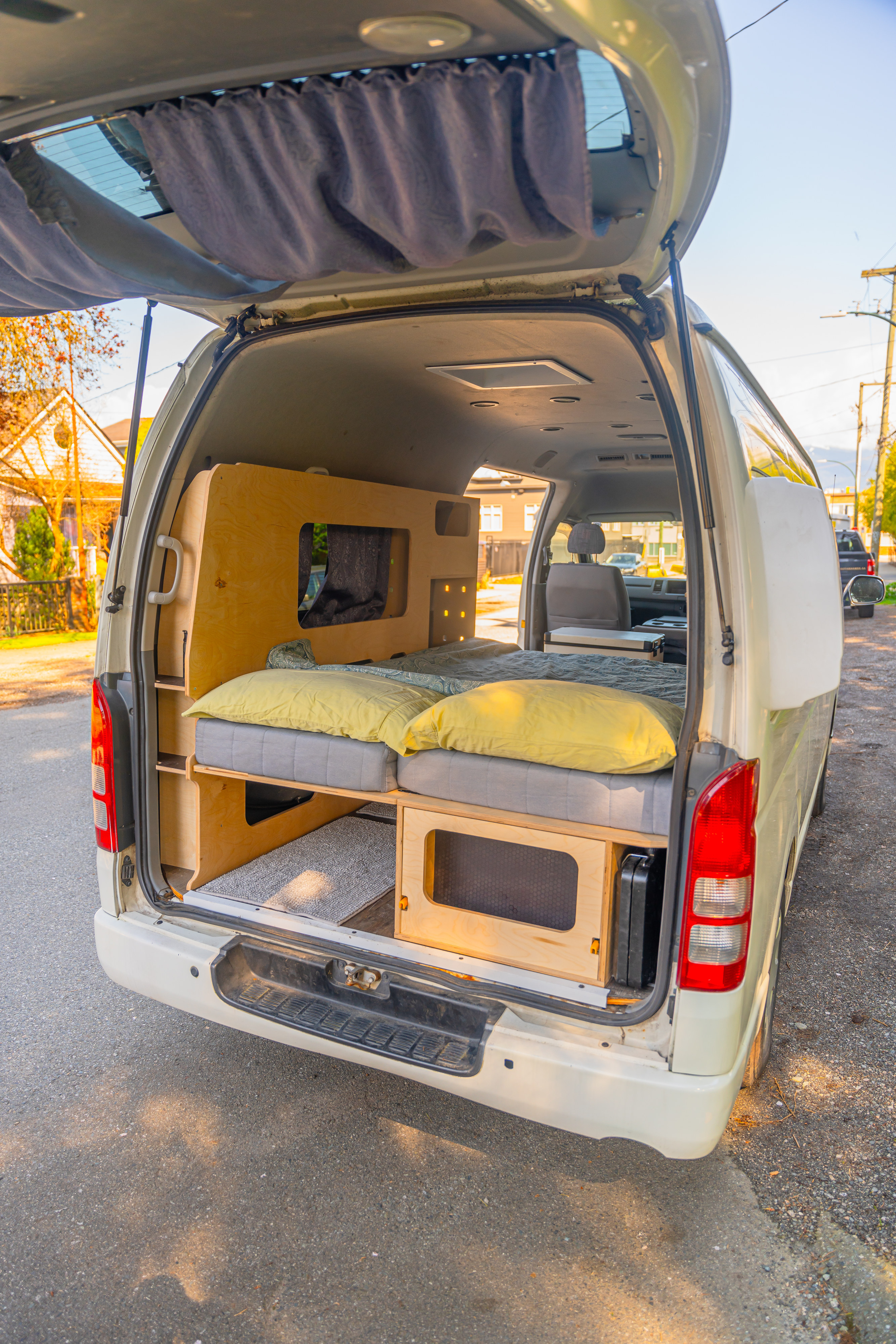 Cozy RV rental: Inside view of a custom camper van conversion with a bed, pillows, & wooden storage.. Toyota Hiace 2005