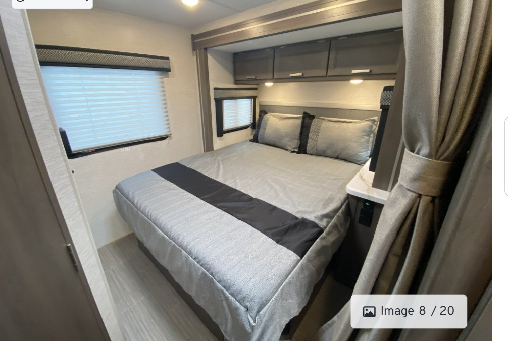 This RV rental bedroom offers a spacious interior with a queen-sized bed, grey bedding, overhead cabinets, and windows with blinds.. Thor Freedom Elite 22FEF 2025