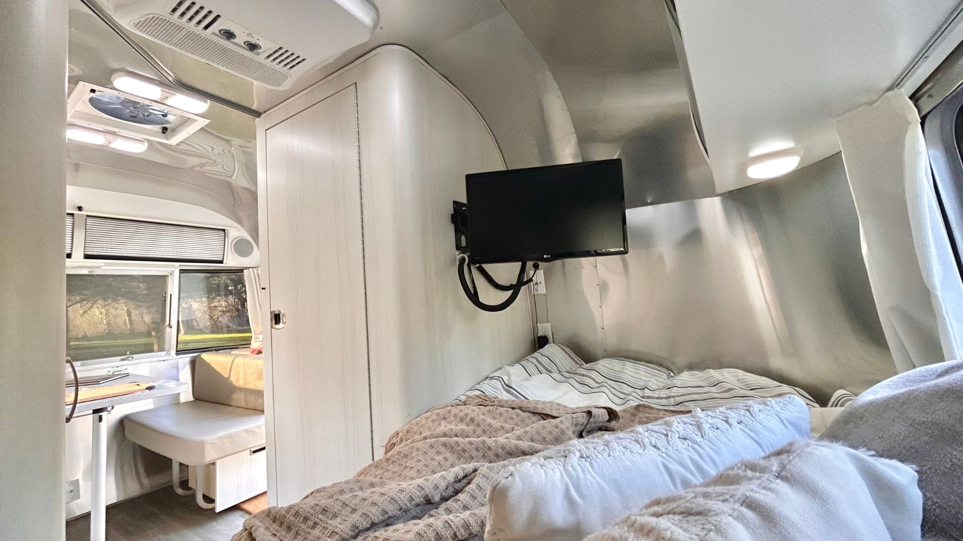 An inviting rv rental interior with a cozy bed, TV, and dinette. Enjoy comfortable travel and views.. Airstream Sport 2018