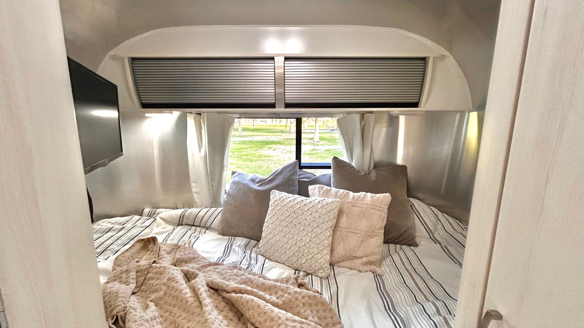 Cozy RV rental bedroom features a comfy bed, TV, and a window with a scenic view outside.. Airstream Sport 2018