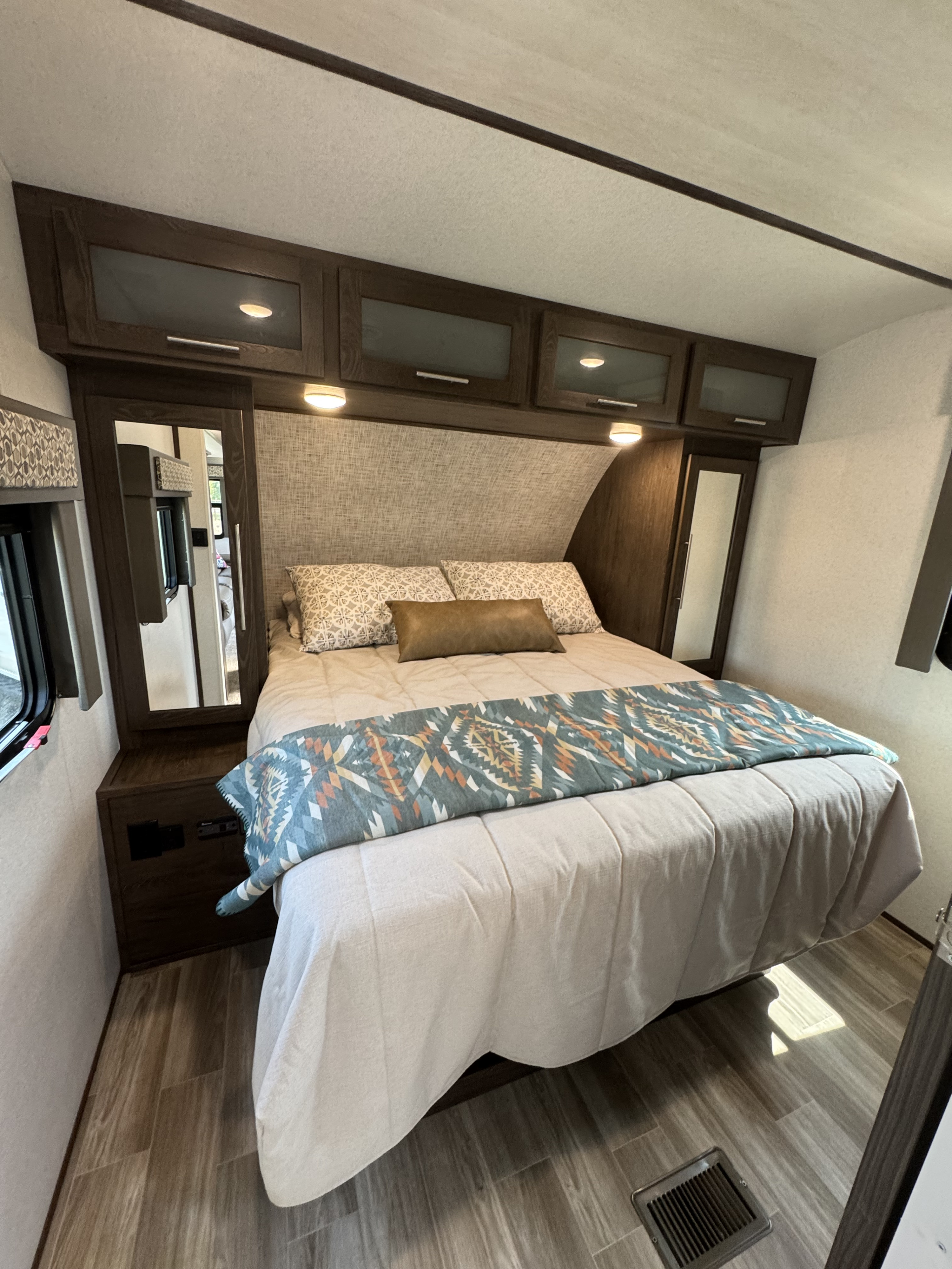 Cozy RV rental bedroom featuring a comfortable bed, overhead storage cabinets, and built-in nightstands with mirrors.. Wildwood Heritage Glen 22RBHL 2019
