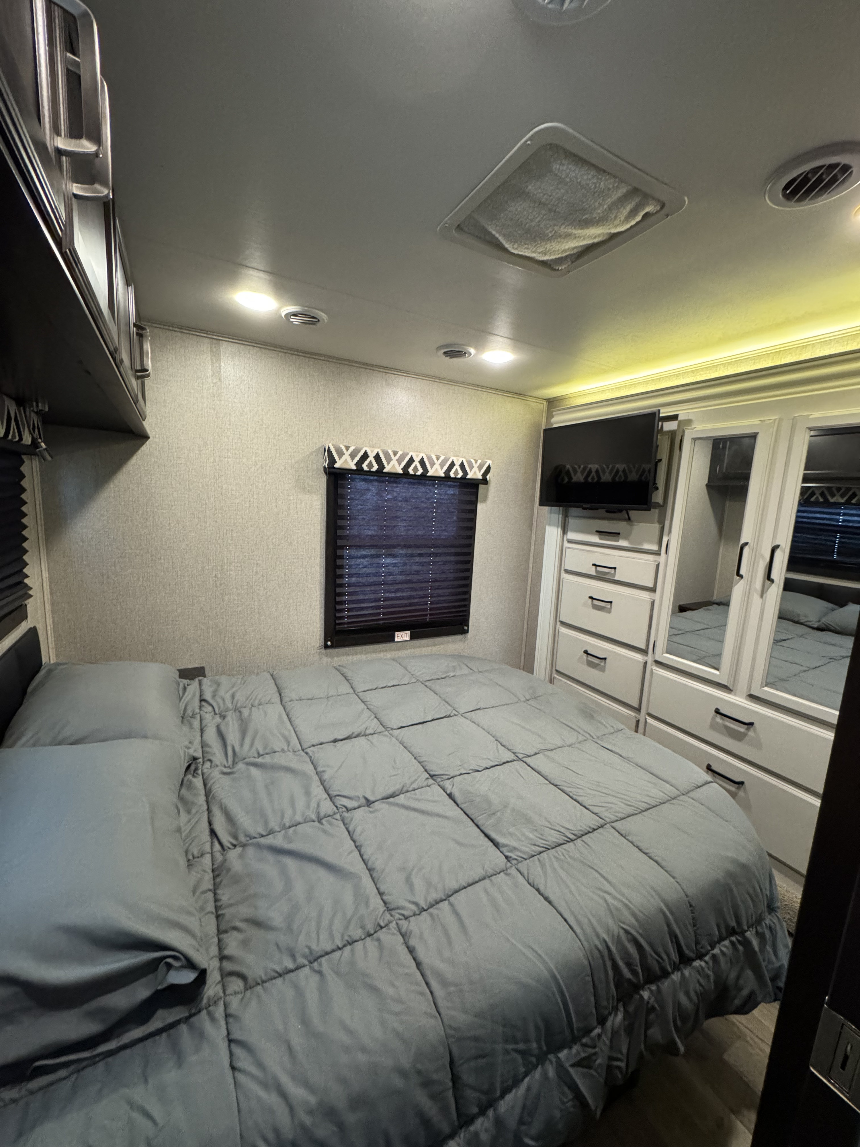 Comfortable RV rental bedroom featuring a gray bed, wall-mounted TV, and mirrored storage on the right.. Entegra Coach Odyssey 2021