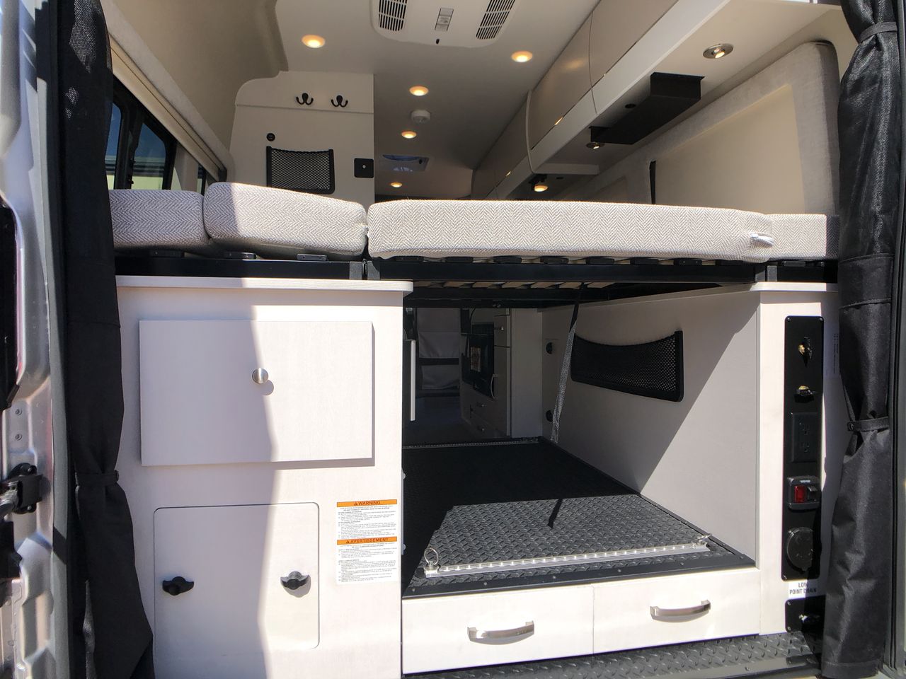 An RV rental interior view from the rear, showing a raised bed, versatile cargo bay, and integrated cabinets.. entegra ethos 2025