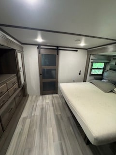Spacious RV rental bedroom: light flooring, queen bed, dresser drawers, & dark-trimmed barn door. Modern RV interior.. Grand Design Grand Design Fifth Wheel 2024