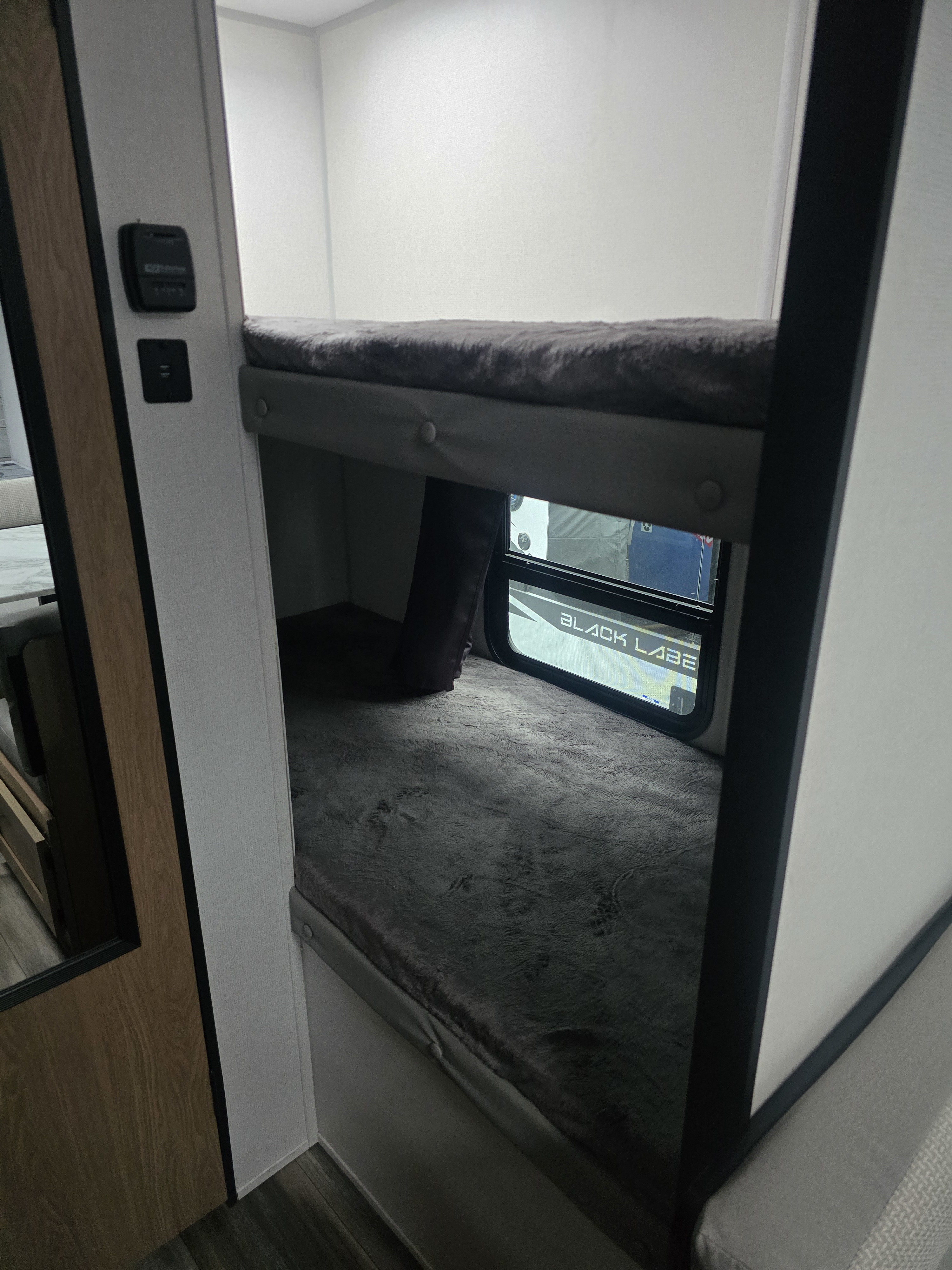 This RV rental features comfortable bunk beds with soft grey bedding, ideal for family travel. Charging port & thermostat visible.. Prime Time Avenger LT 16BH 2023
