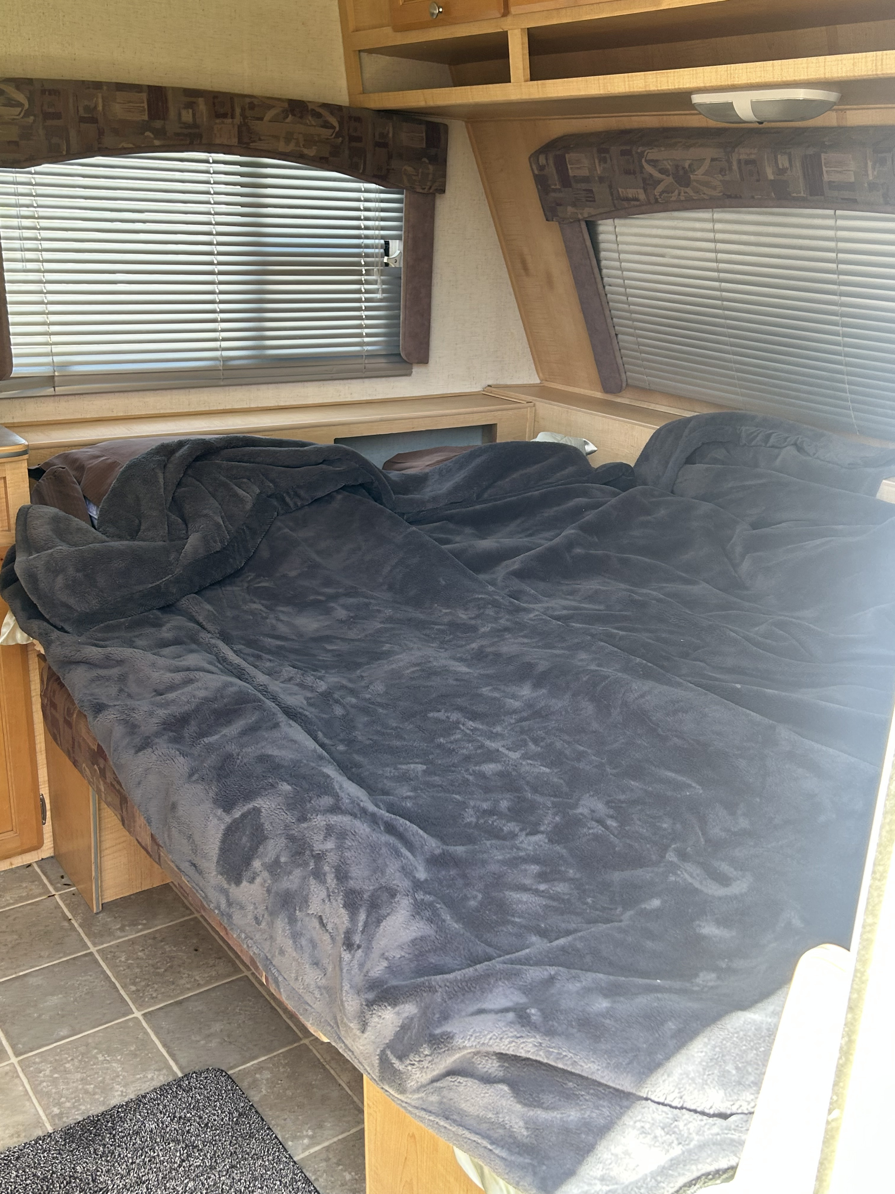 Cozy RV rental bedroom with a dark grey blanket on the bed, flanked by windows with blinds and wood trim.. R-Vision Trail-Lite 2005