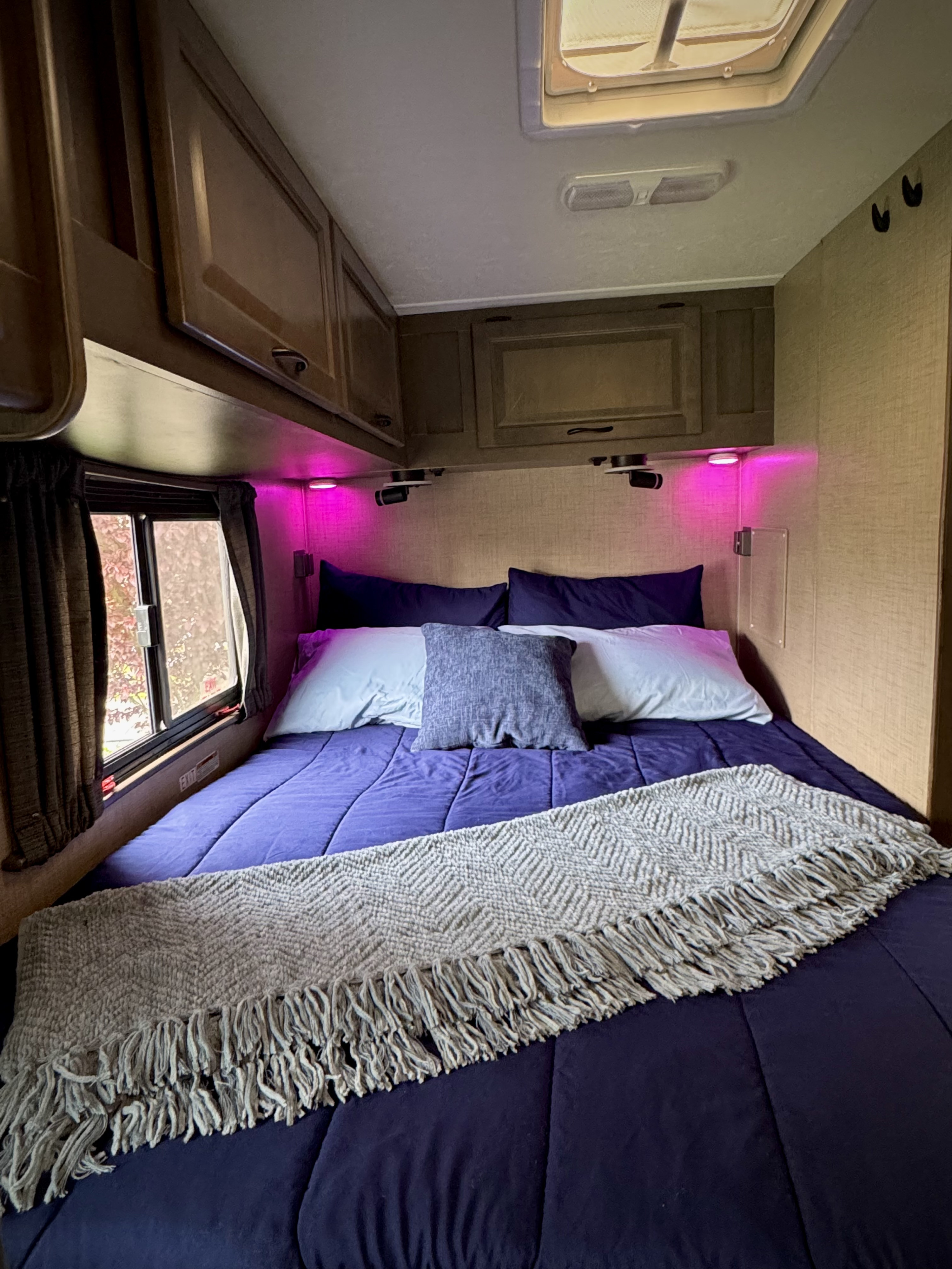 Cozy RV rental bedroom with purple bedding, overhead cabinets, and pink accent lighting.. Thor Majestic 2019