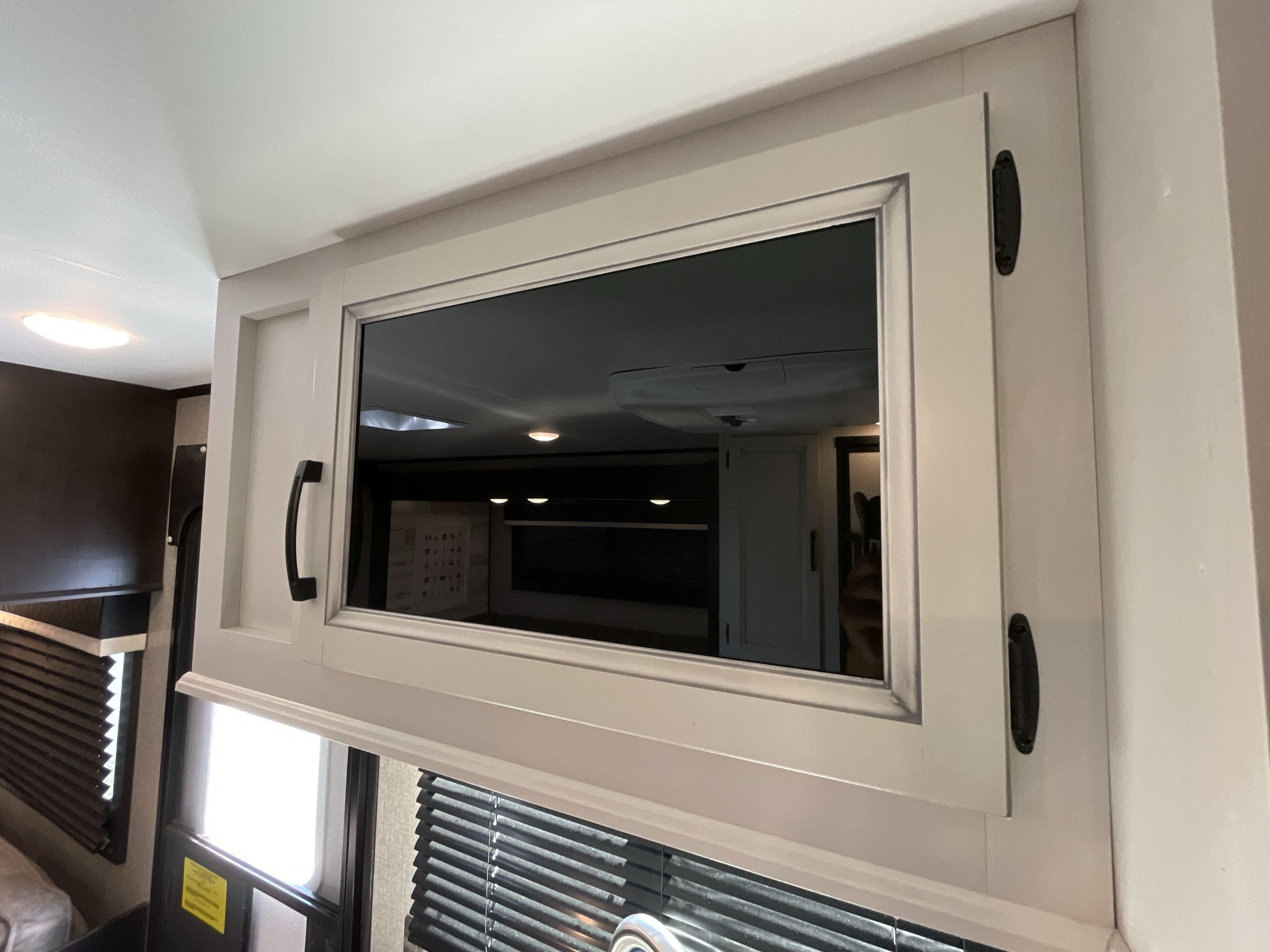 Bright, modern RV rental interior featuring an overhead cabinet with reflective glass revealing additional lighting and space.. Jayco Jay Feather 2020