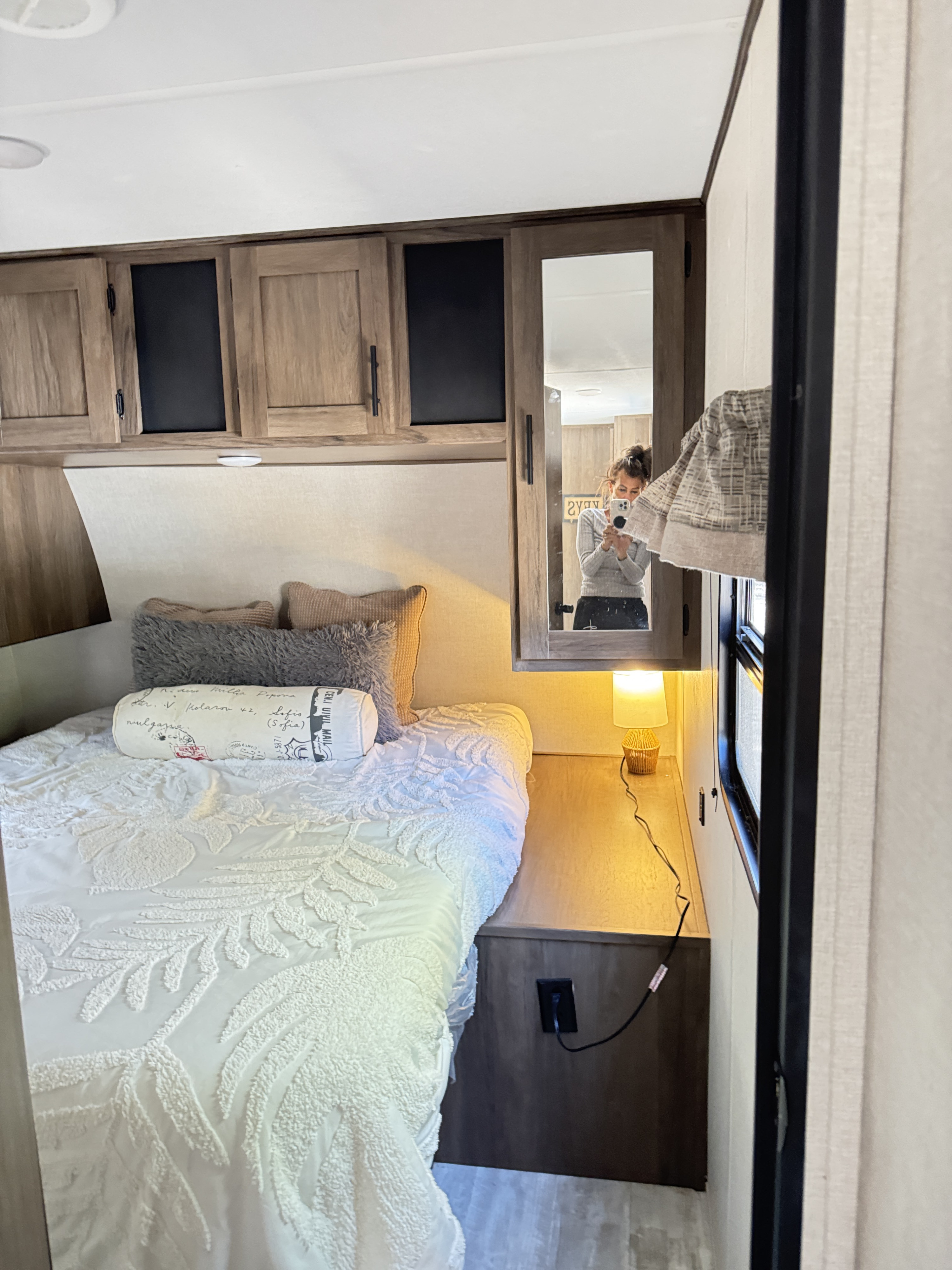 Cozy RV rental bedroom with white bedding, overhead cabinets, and a reflected view of the photographer in the mirror.. Avenger Avenger Trailer 2021