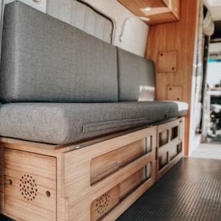 Inside our RV rental, a modern camper van offers a plush grey convertible bed & sleek wooden storage drawers. Perfect for trips!. Mercedes-Benz Sprinter RV Motorhome Campervan 2020