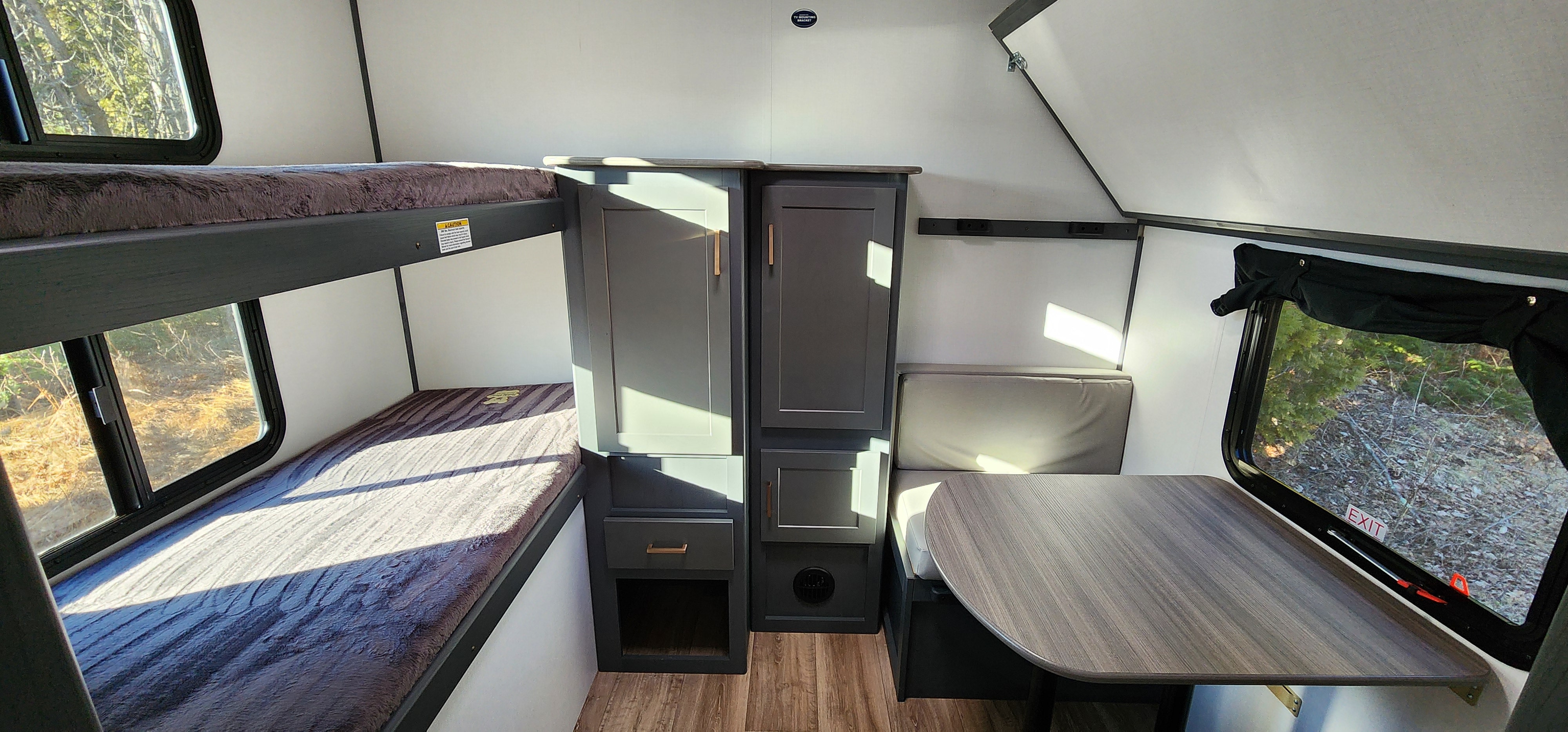 Cozy RV rental interior with bunk beds, dinette, and ample storage cabinets. Sunlight streams through windows, highlighting the living space.. Keystone RV Bullet Ultra Lite 2023