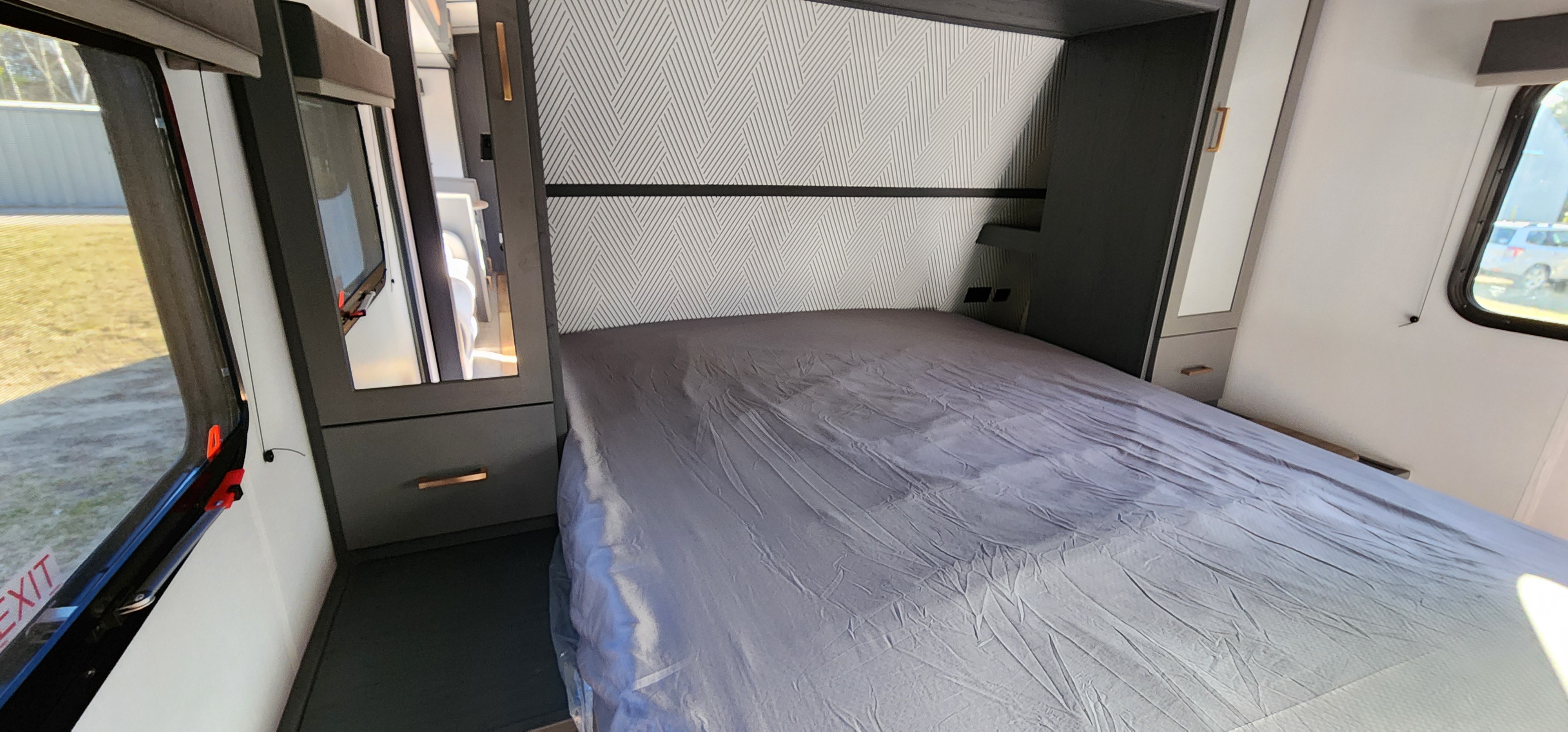 This RV rental showcases a comfortable bedroom with a grey-sheeted bed, patterned wall, and sleek dark cabinets.. Keystone RV Bullet Ultra Lite 2023
