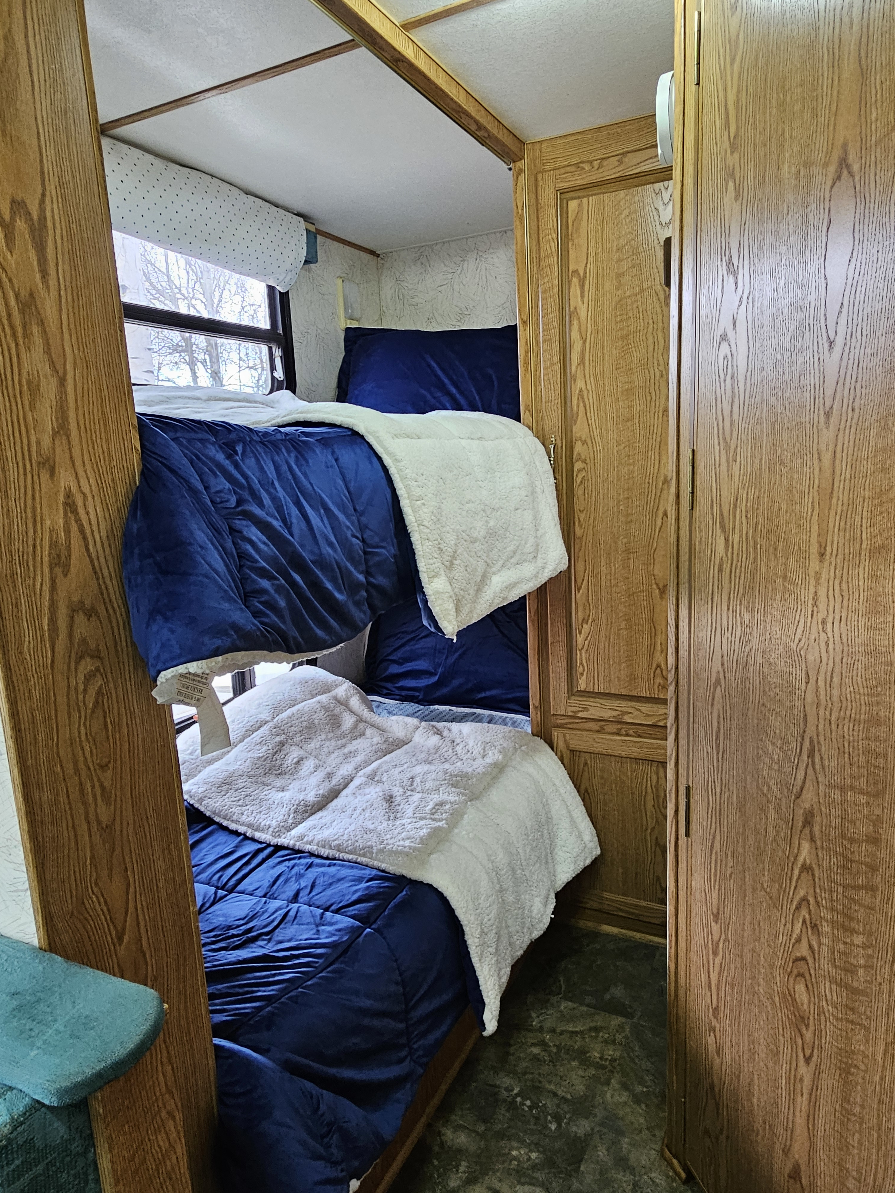 Cozy RV rental interior featuring comfortable navy bunk beds with soft white blankets & wood paneling, ready for your trip.. Kit Sunchaser 1994