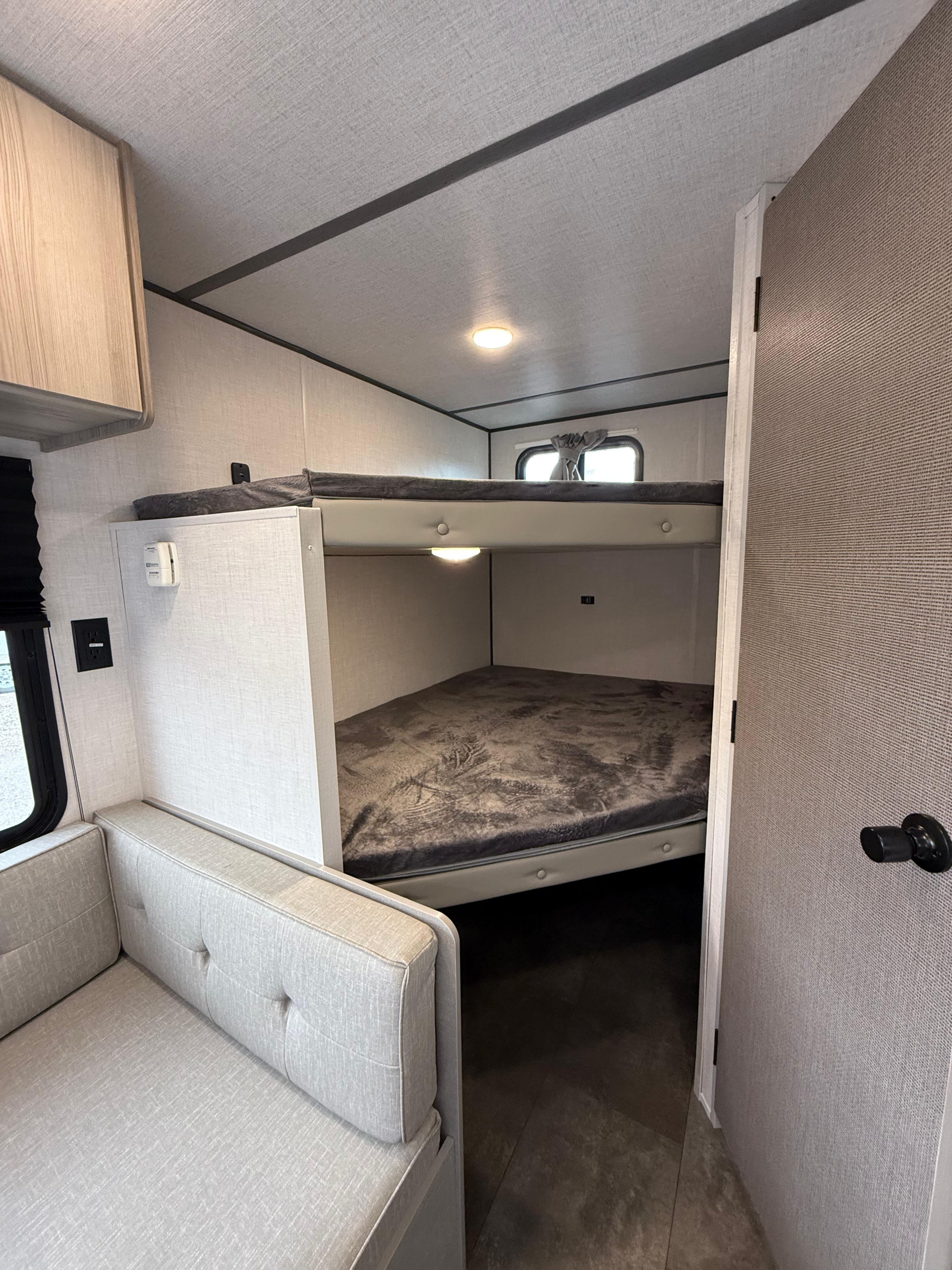 This modern RV rental interior features a cozy bunk bed setup and a comfortable light-grey sofa, ideal for camper adventures.. Forest River Wildwood FSX 2025