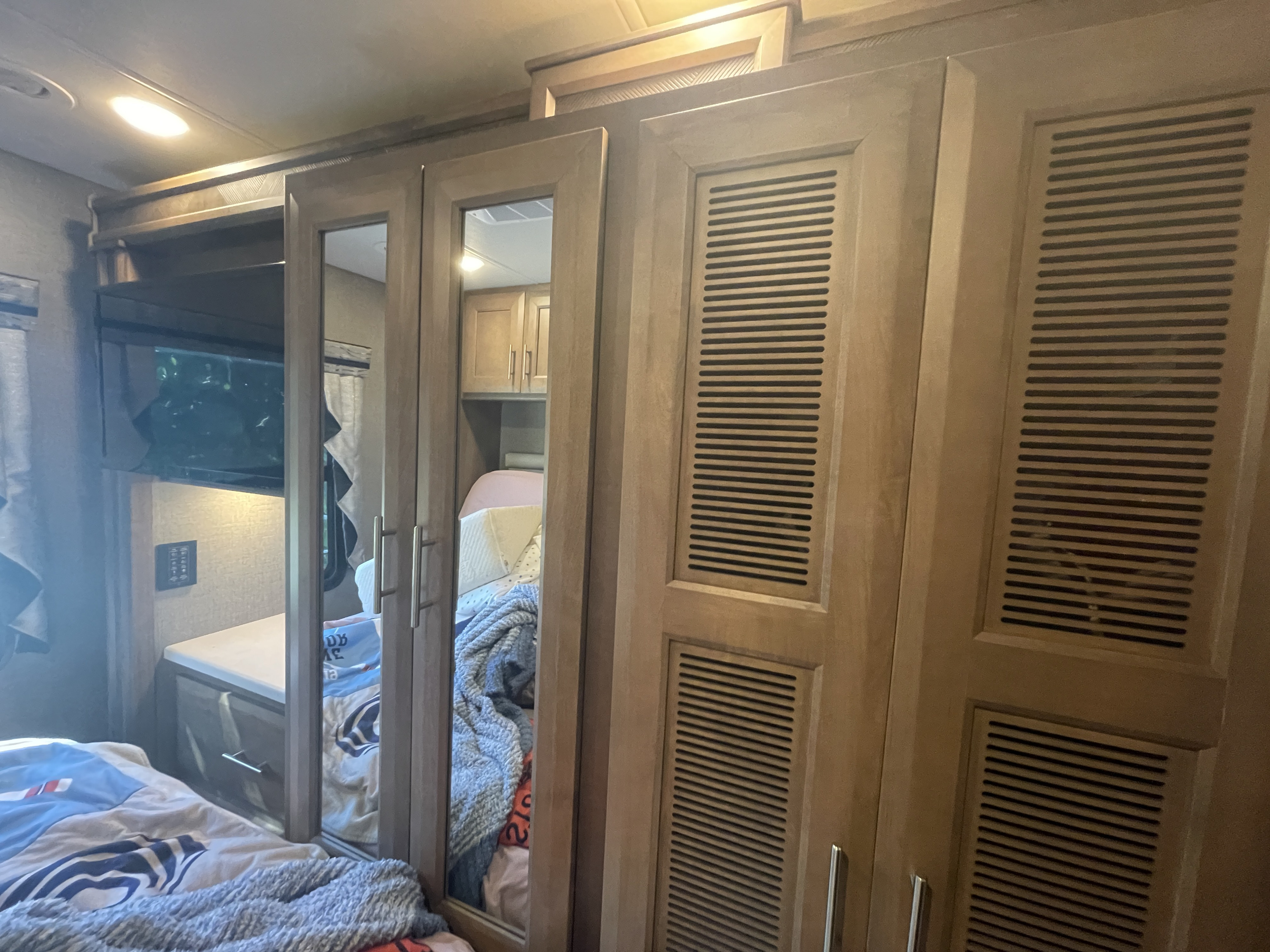 RV rental bedroom: wooden cabinetry, slatted vents, mirrored doors reflecting a bed, and a wall-mounted TV.. Mirimar 34.8 2022