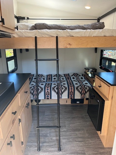 RV rental interior: upper bunk with ladder, lower bed, compact kitchen, and storage cabinetry.. Elusive Lo Pro Cabin 2023