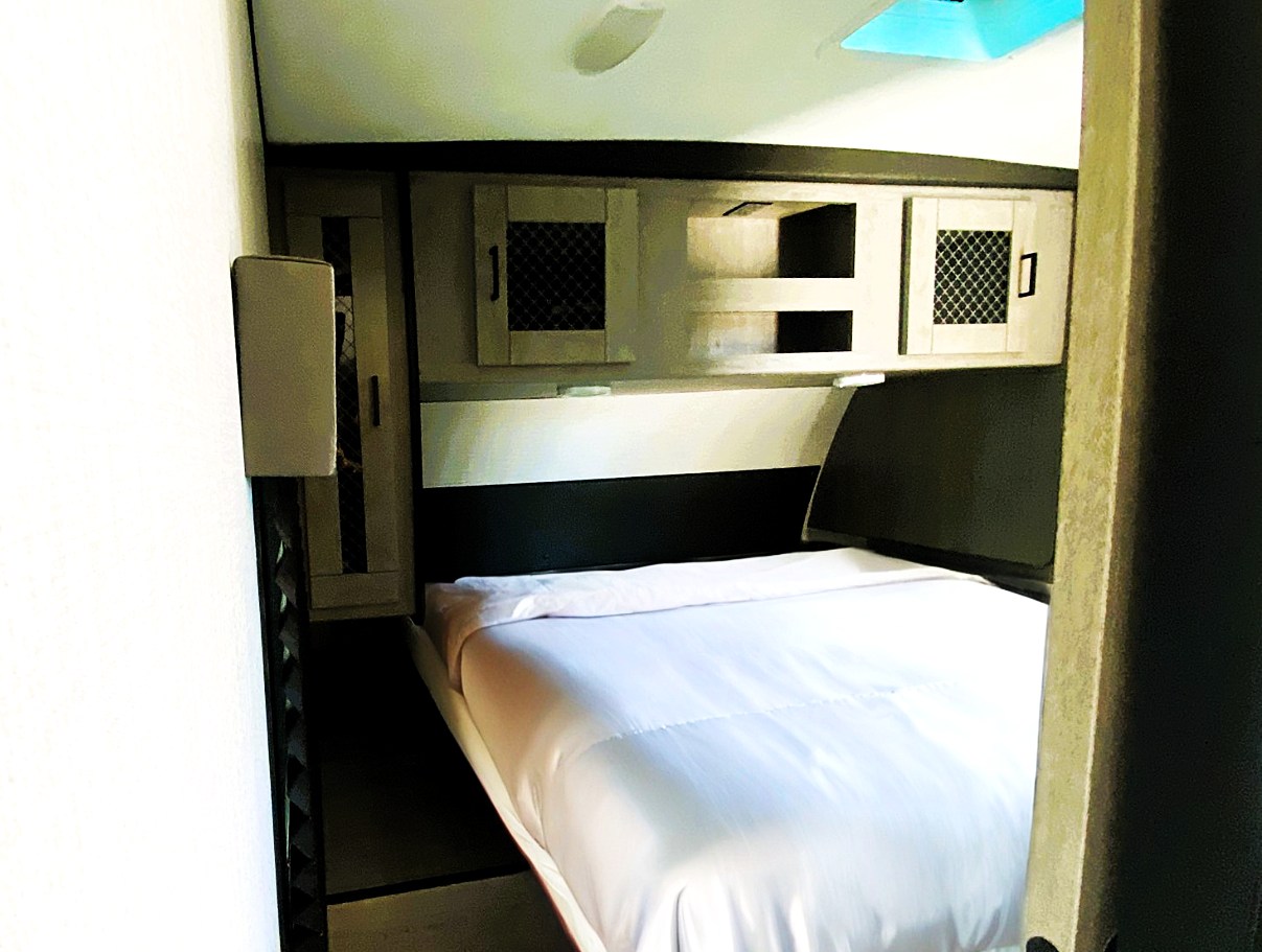 Compact RV rental bedroom with a tidy bed, white sheets, and practical overhead cabinets.. Heartland RVs Mallard 2021