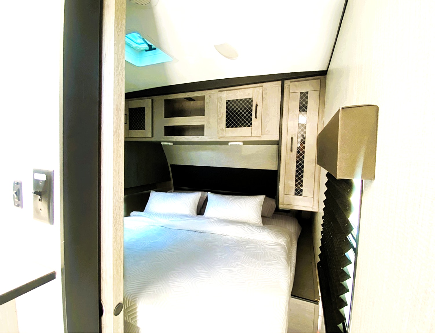 This rv rental bedroom features a comfortable white bed, overhead cabinets, and a skylight, offering a compact, cozy space.. Heartland RVs Mallard 2021