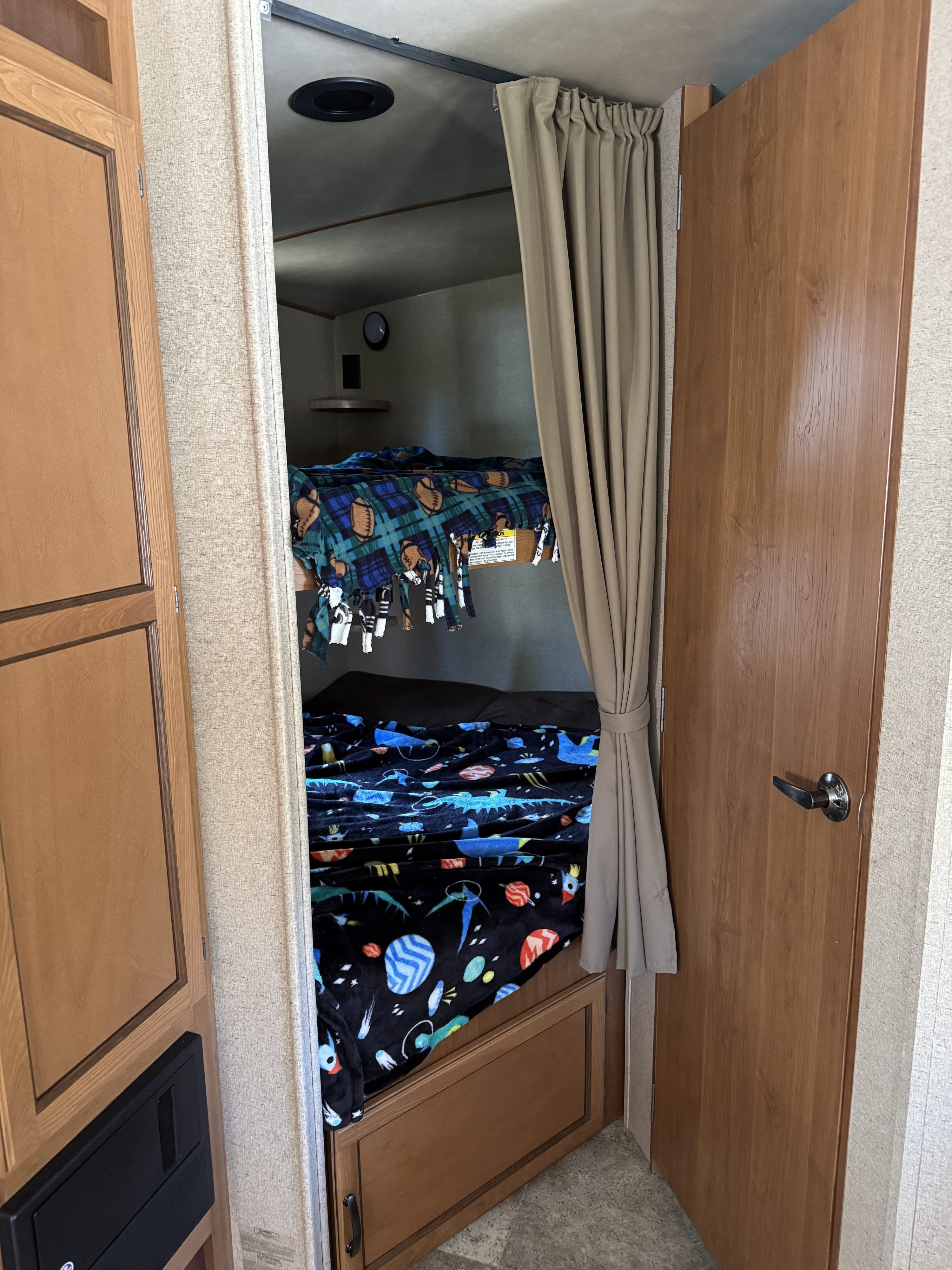 Cozy bunk beds in an RV rental, with fun themed blankets, a pulled-back privacy curtain, and wood interior.. Crossroads RV Sunset Trail Super Lite 2017