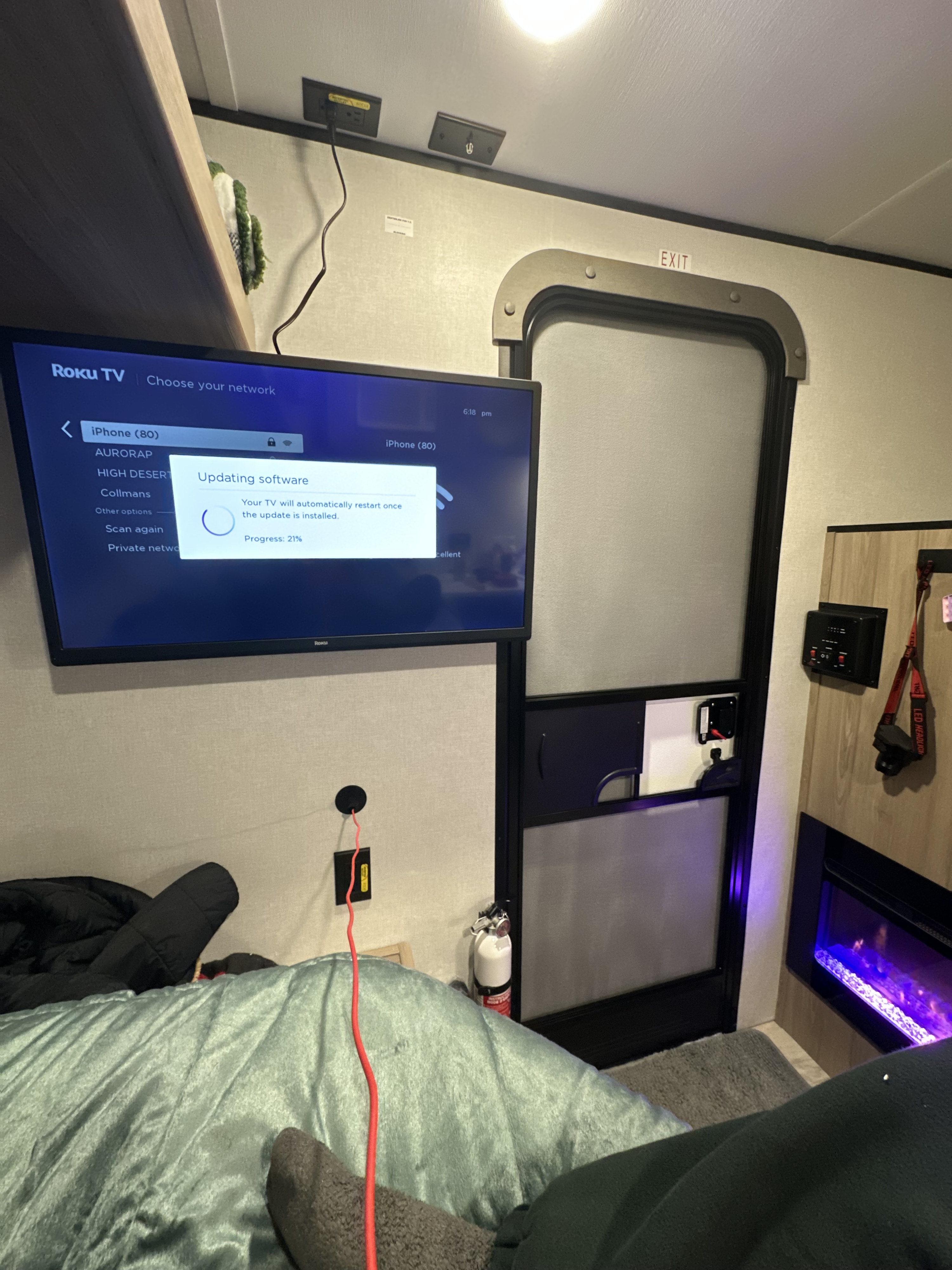 Roku TV updating in a cozy RV rental interior, featuring a soft bed, an exit door, and an electric fireplace.. Coleman 13C 2025