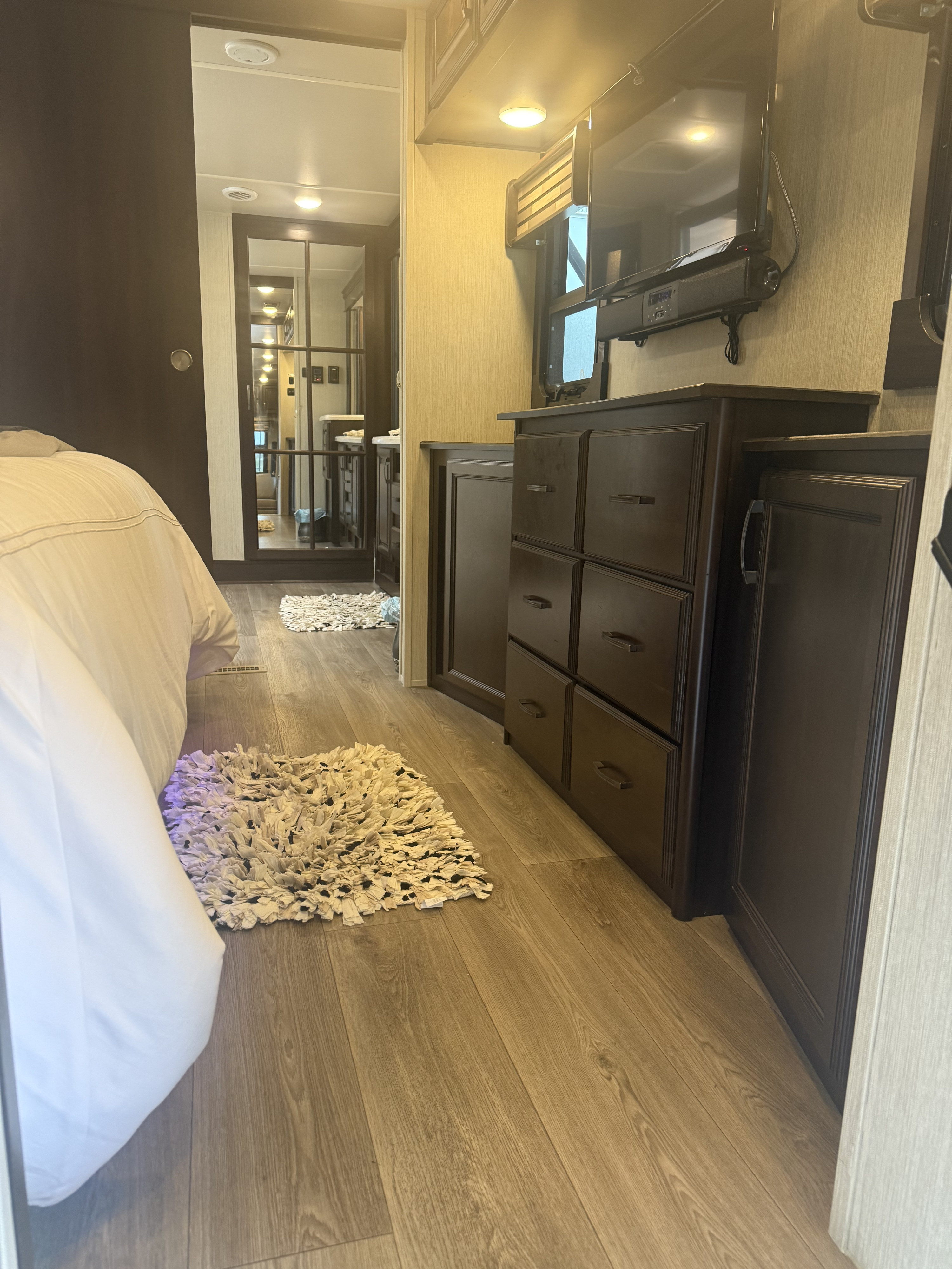Modern RV rental bedroom with wood floors, plush rug, dark dresser, and TV. A mirrored door reflects the hallway.. Forest River Palomino Columbus 2018