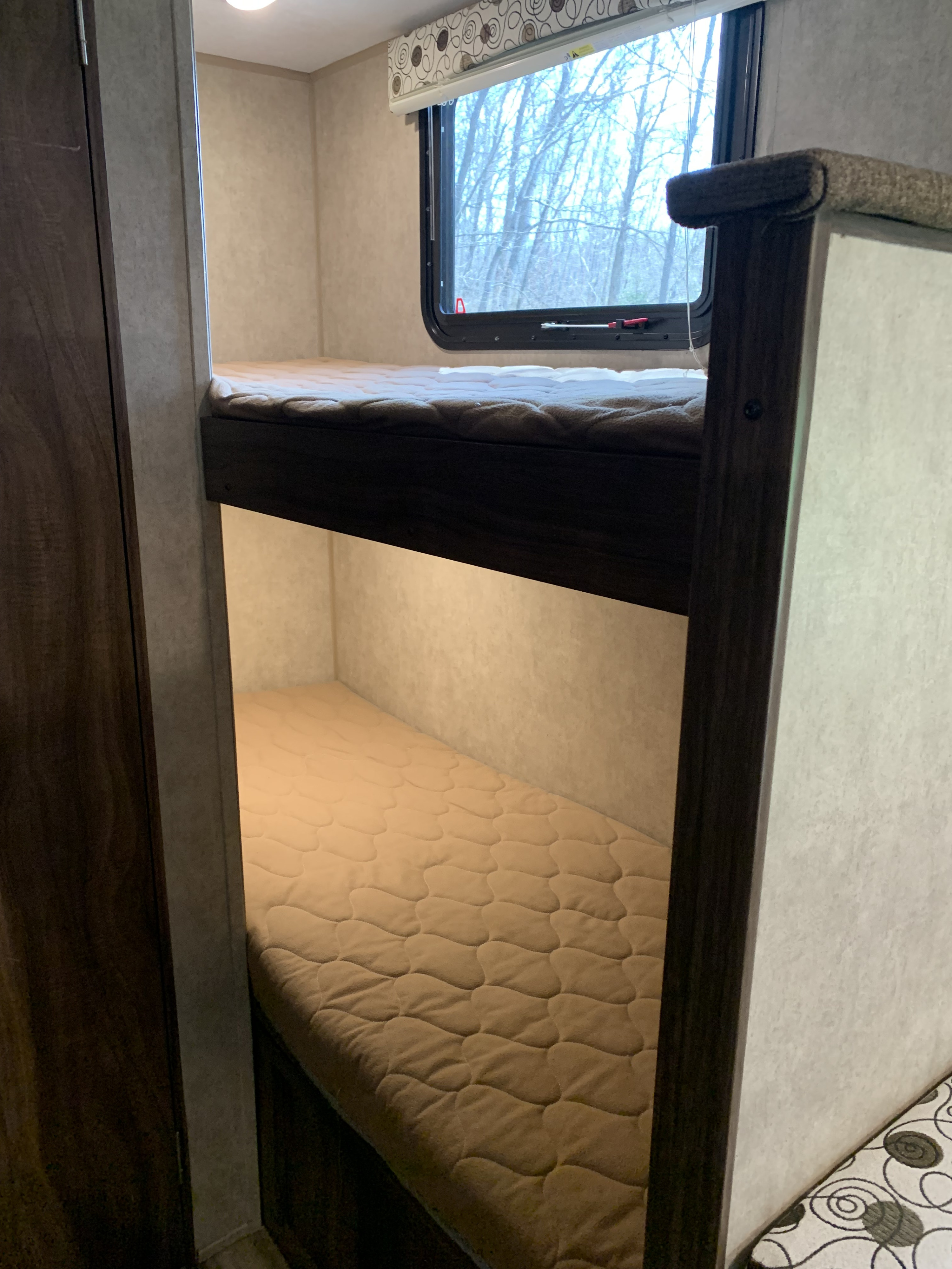 Inside an RV rental: two cozy bunk beds with quilted mattresses, a window, and soft under-bunk lighting.. Clipper Cadet 2018