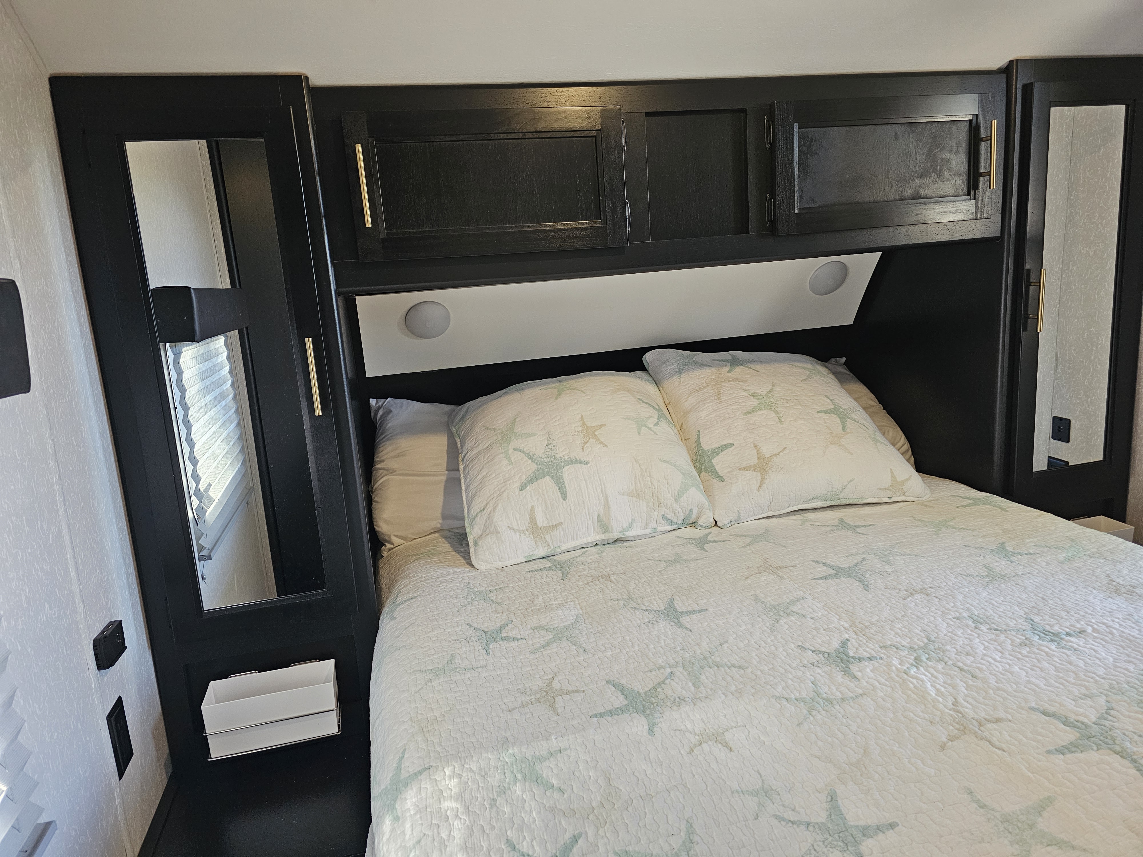 Cozy RV rental bedroom featuring a bed with starfish bedding, overhead cabinets, and built-in lighting.. Forest River Cherokee Grey Wolf 2022