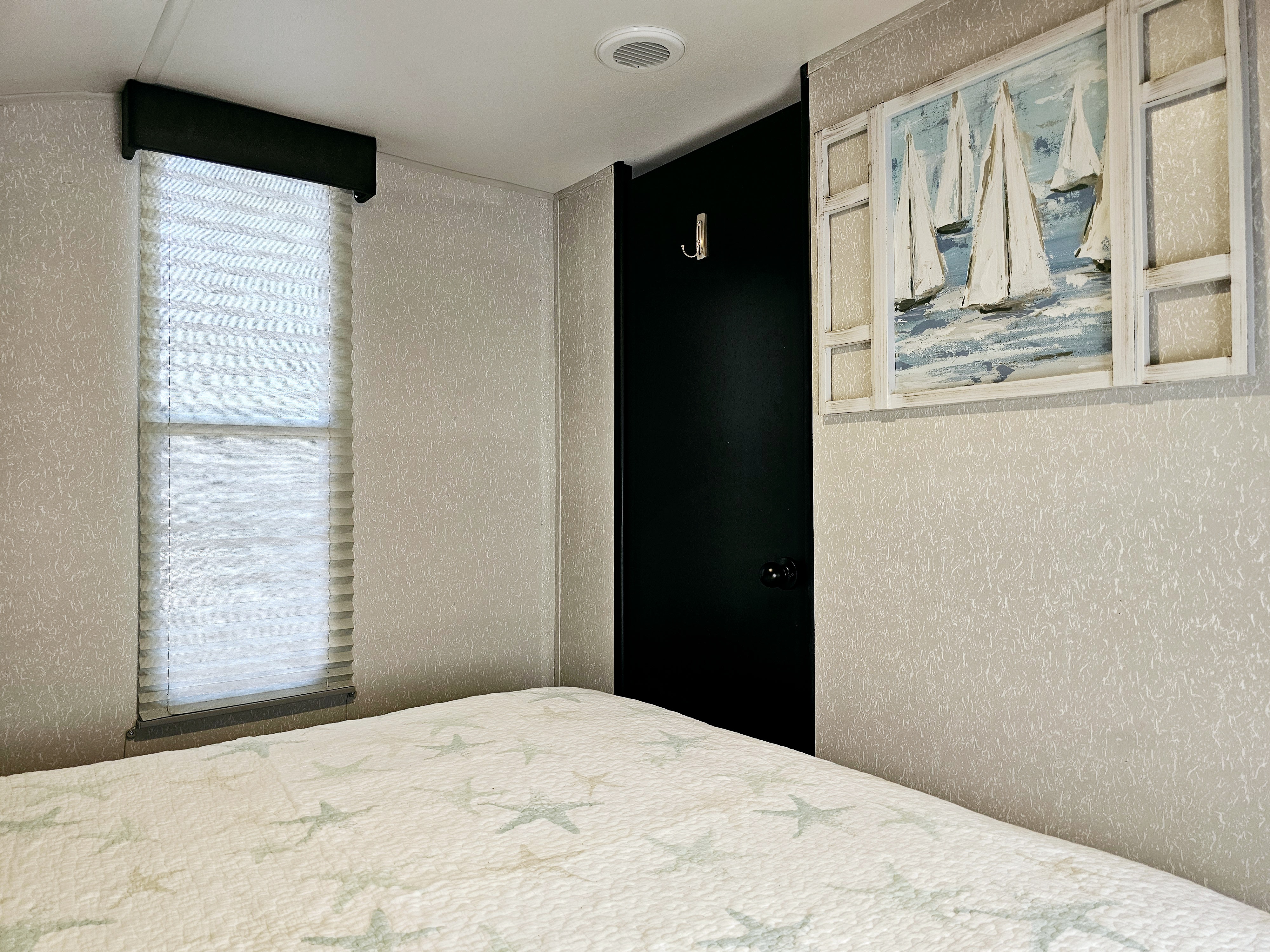 Cozy RV rental bedroom with starfish quilt, window, dark door, and sailboat art, perfect for travel.. Forest River Cherokee Grey Wolf 2022