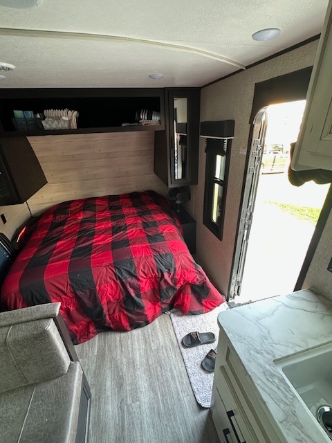 This RV rental interior features a cozy bedroom with red and black plaid bedding, a compact kitchen, and seating.. Jayco Jay Flight 2023