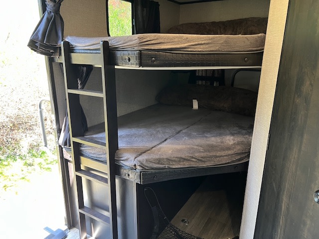 Interior of an RV rental showing multi-level bunk beds with dark grey mattresses, a ladder, and a window view.. Jayco Jay Feather 2022