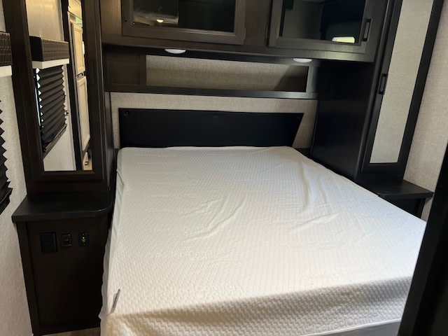 Cozy RV rental bedroom with a comfortable bed, overhead storage, and integrated bedside amenities.. Jayco Jay Feather 2022