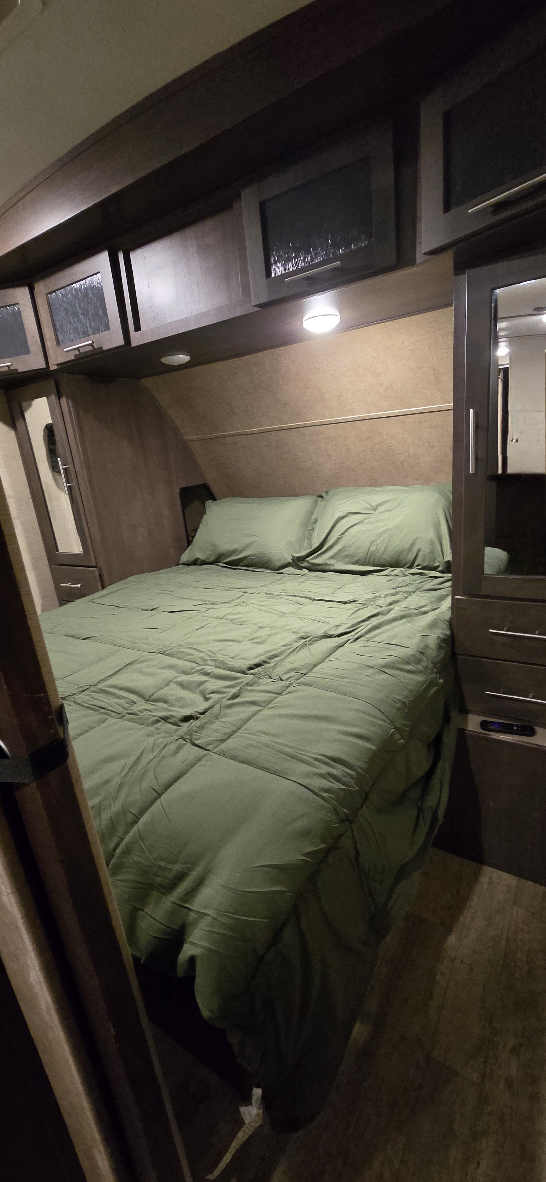 Compact RV rental bedroom featuring a green-sheeted bed, pillows, and built-in wooden cabinetry. Perfect for travel.. Forest River Surveyor 2016